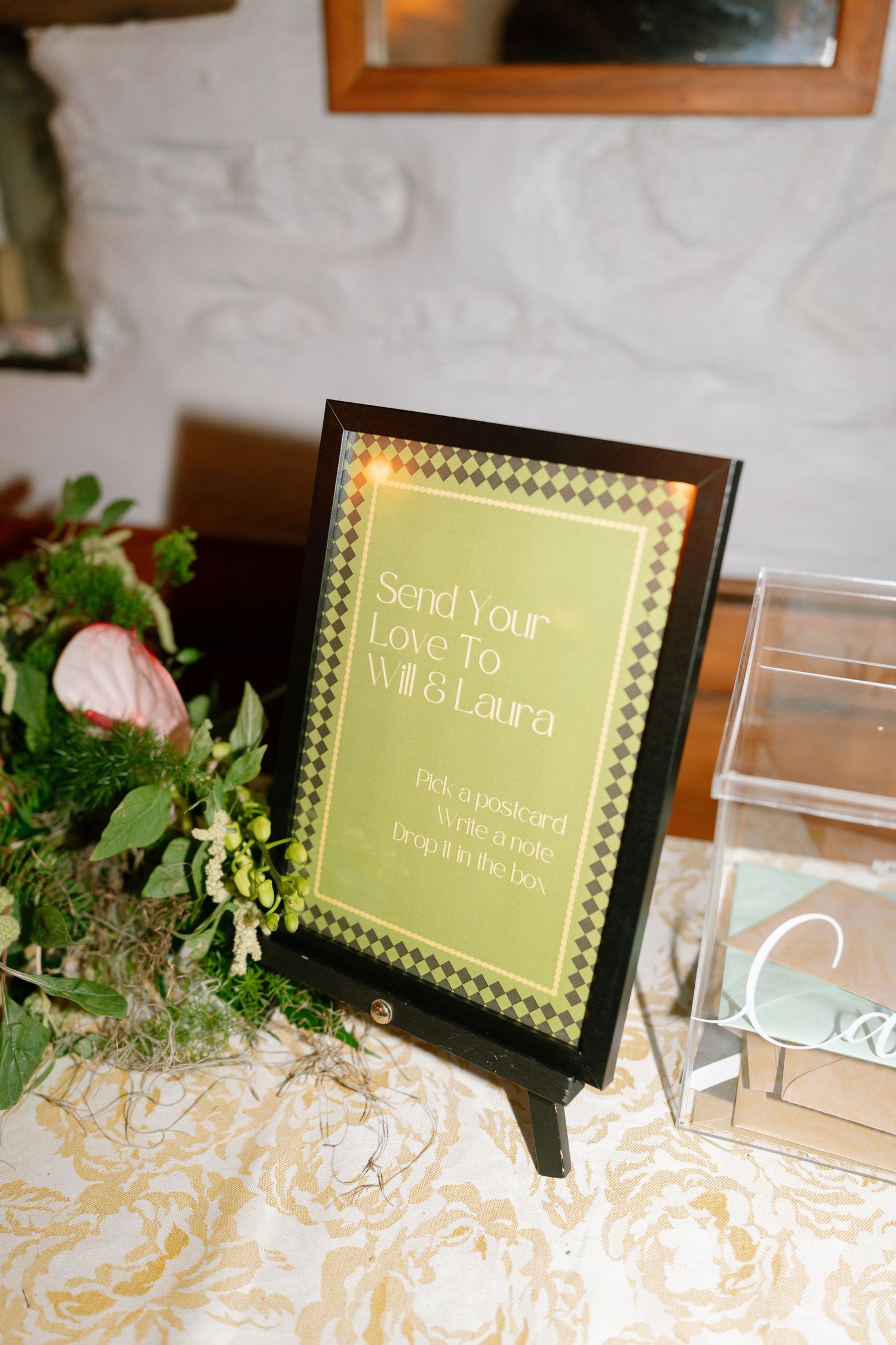 Wedding reception table decor with framed signs and decorative greenery on a textured tablecloth.