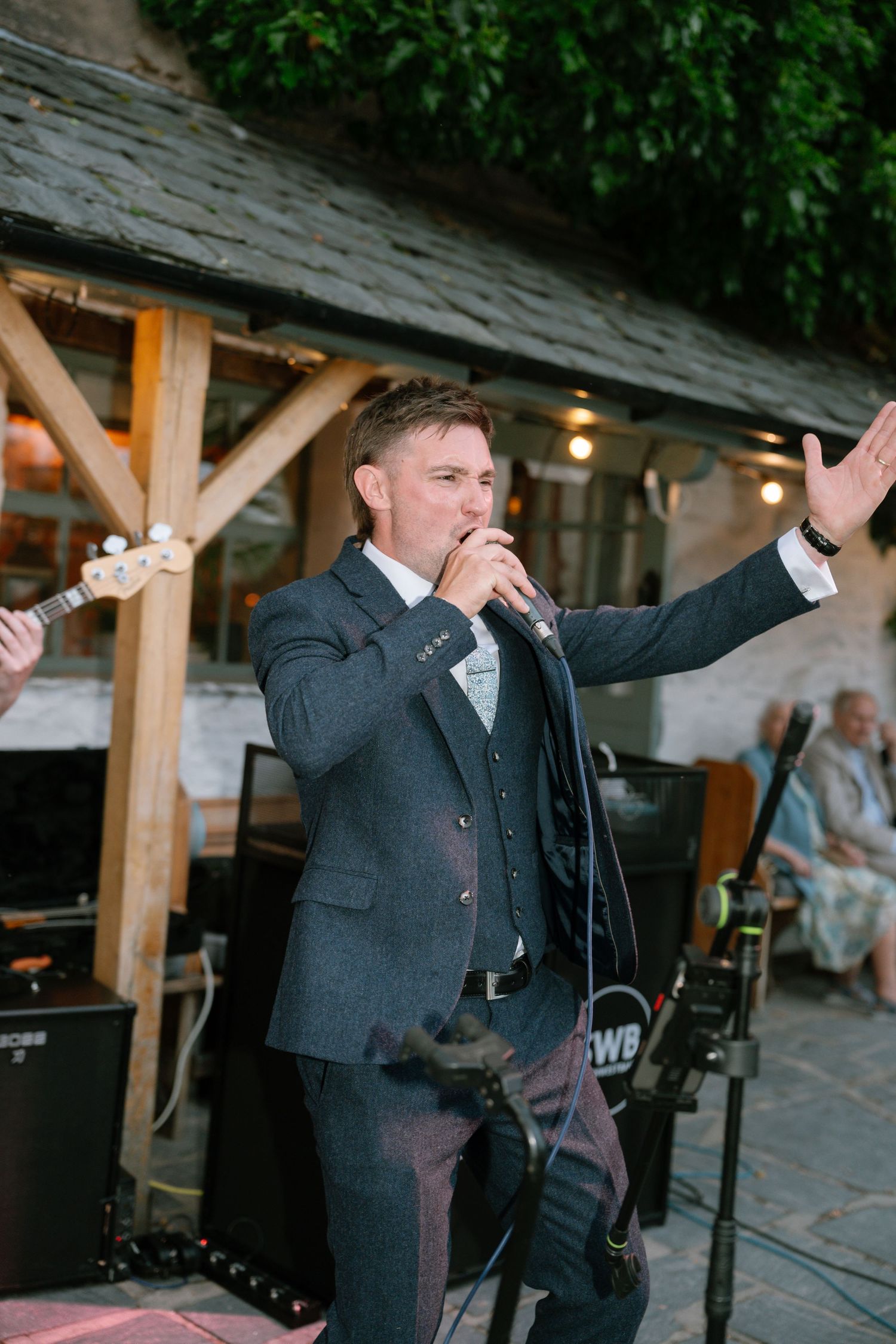 Person in suit gestures enthusiastically while performing at outdoor venue.