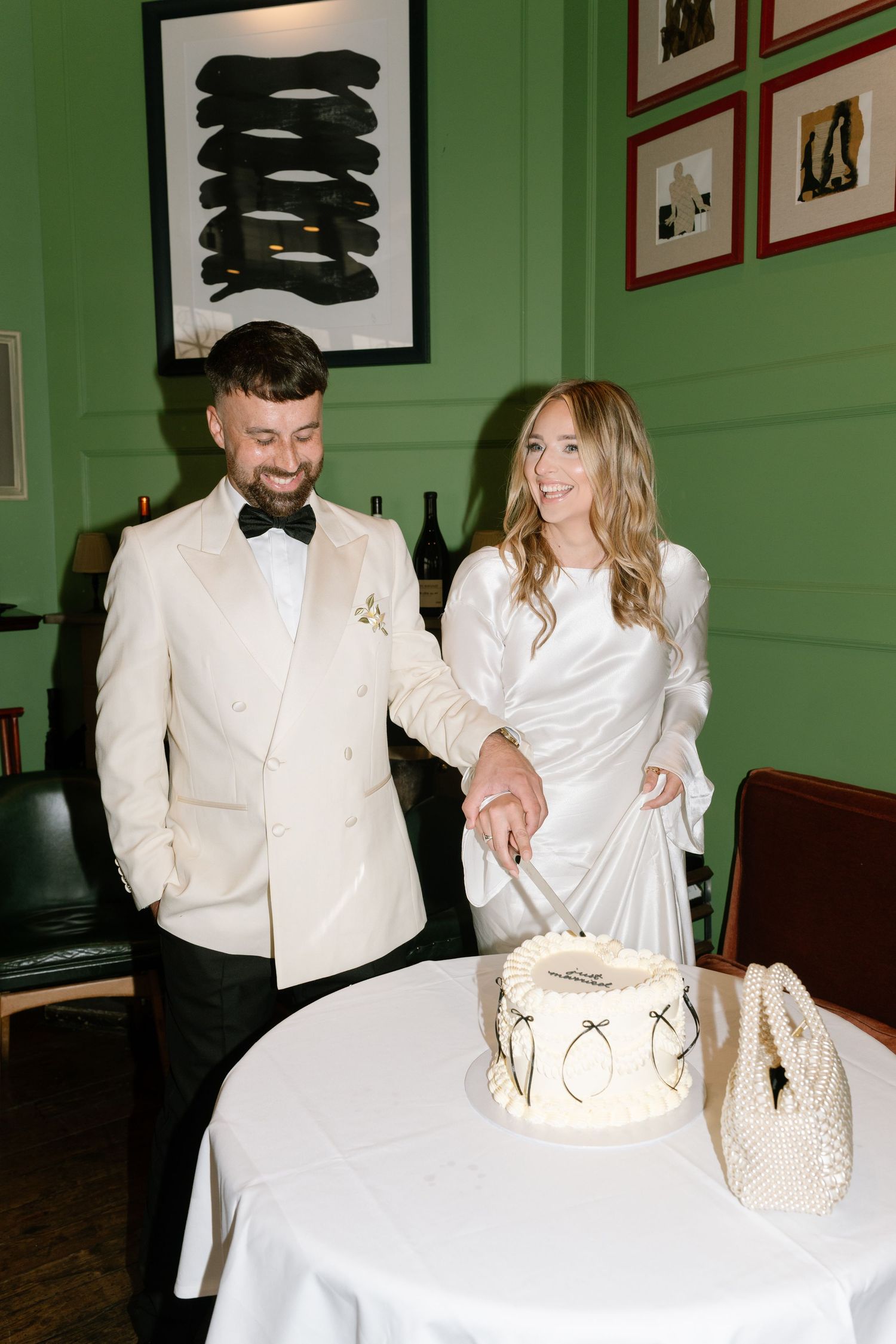 Wedding couple in white formal attire share a joyful moment while cutting their minimalist white cake.
