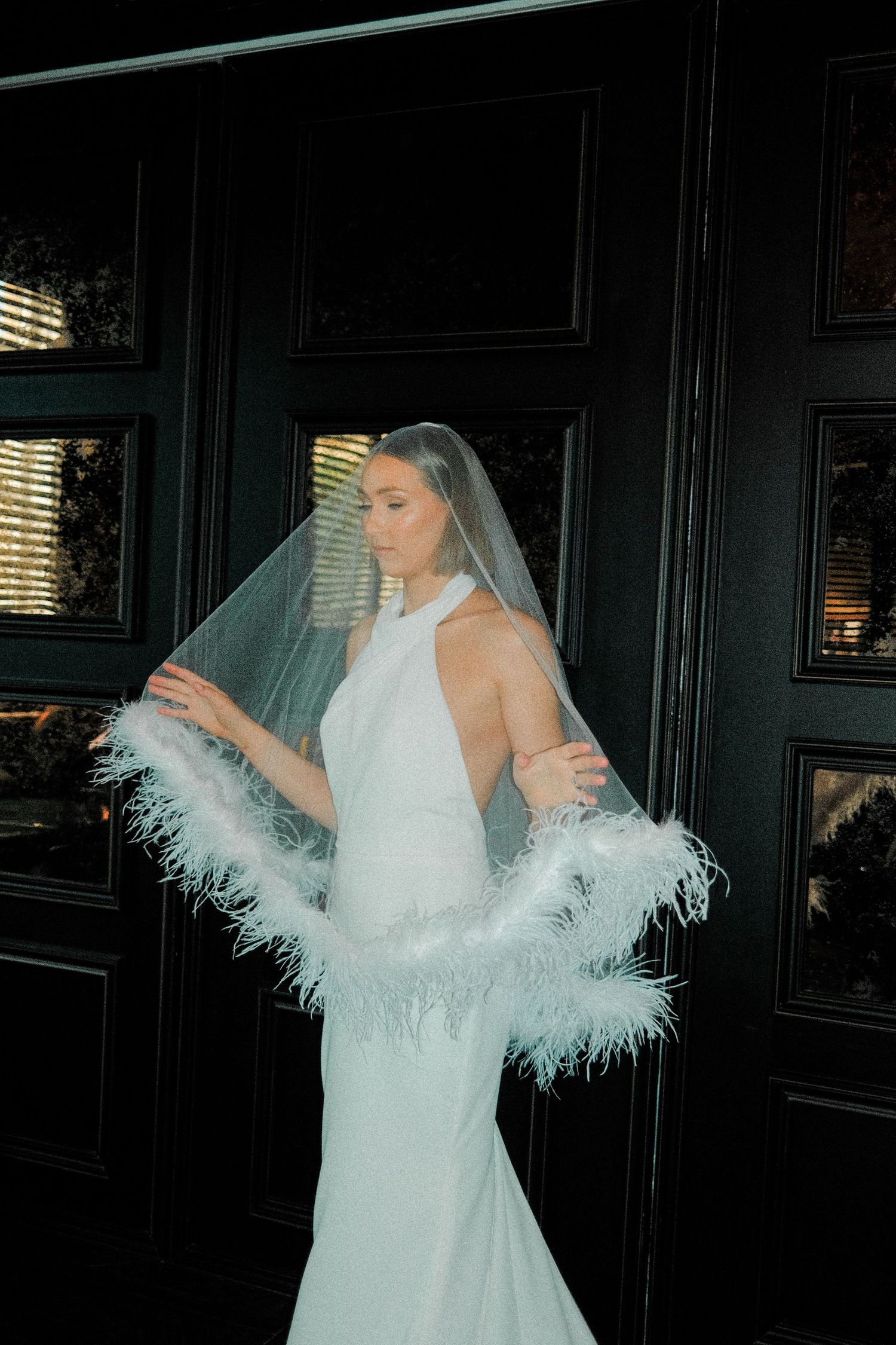 Elegant white wedding gown with feather boa details and halter neckline photographed against dark paneled walls.
