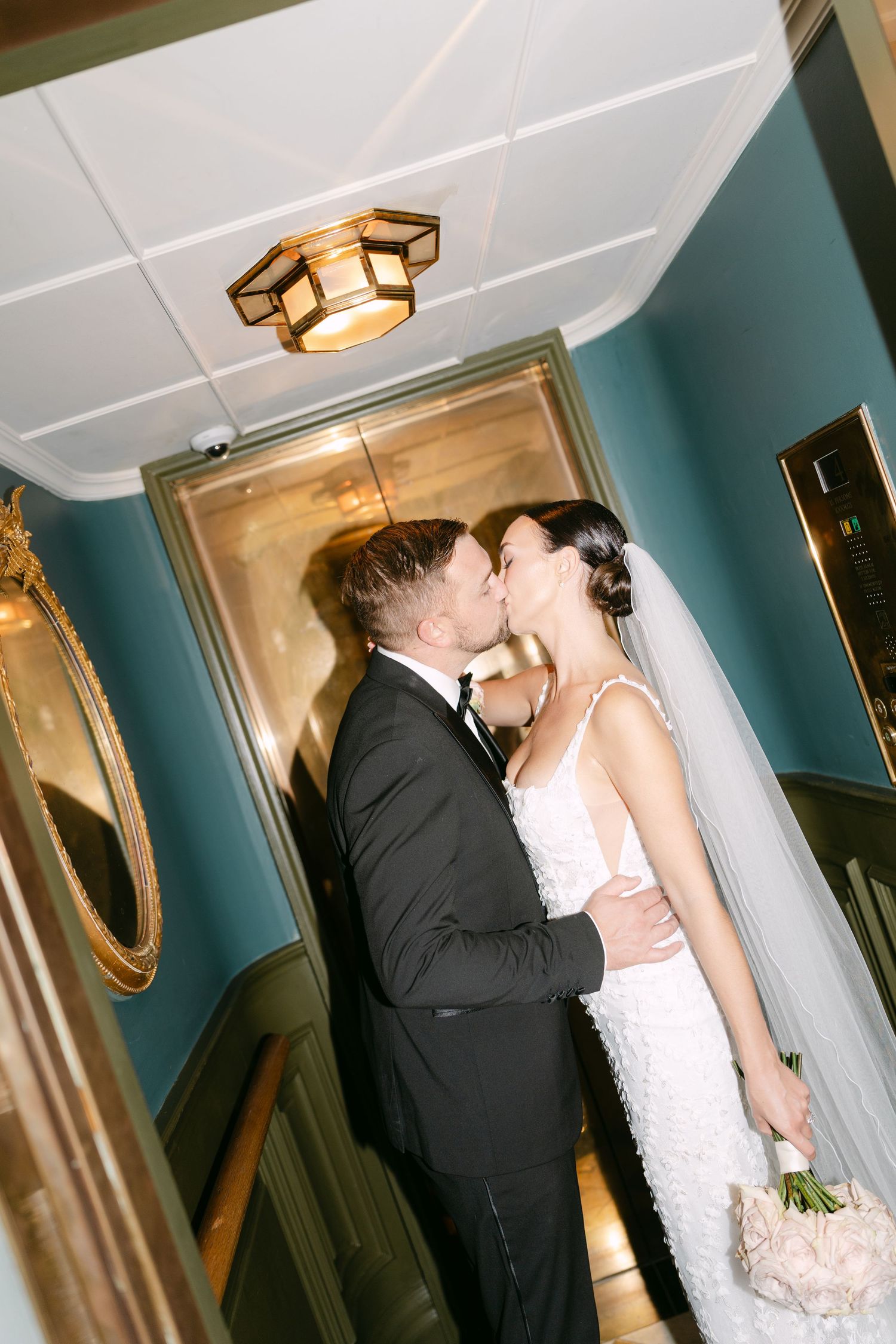 Wedding couple shares an intimate moment in an elevator with teal walls and gold accents.