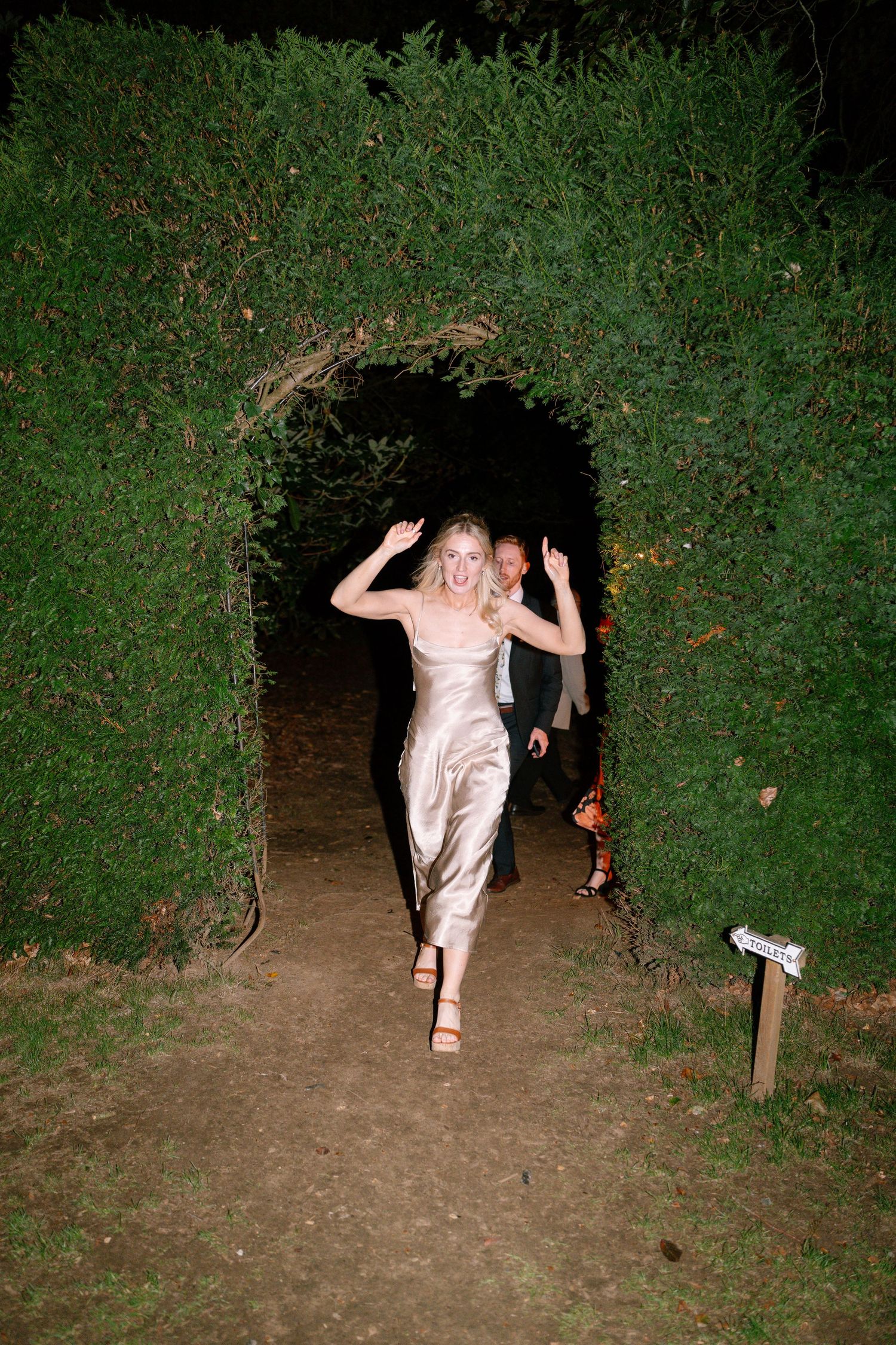 Person in formal attire running through a garden path at night.