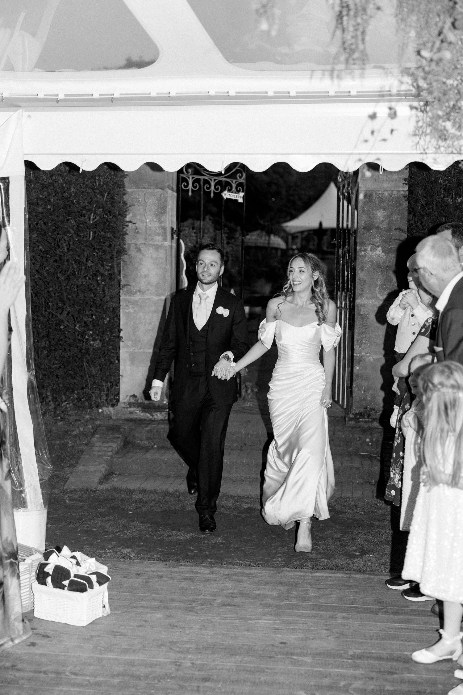 Couple making grand entrance through decorated archway at wedding celebration.
