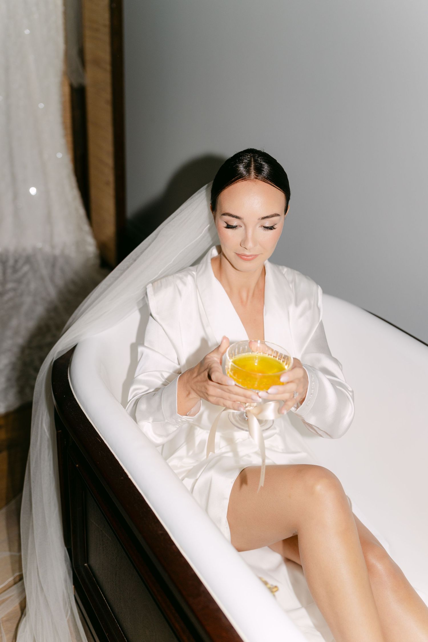 Person in white robe relaxing in bathtub with orange juice.