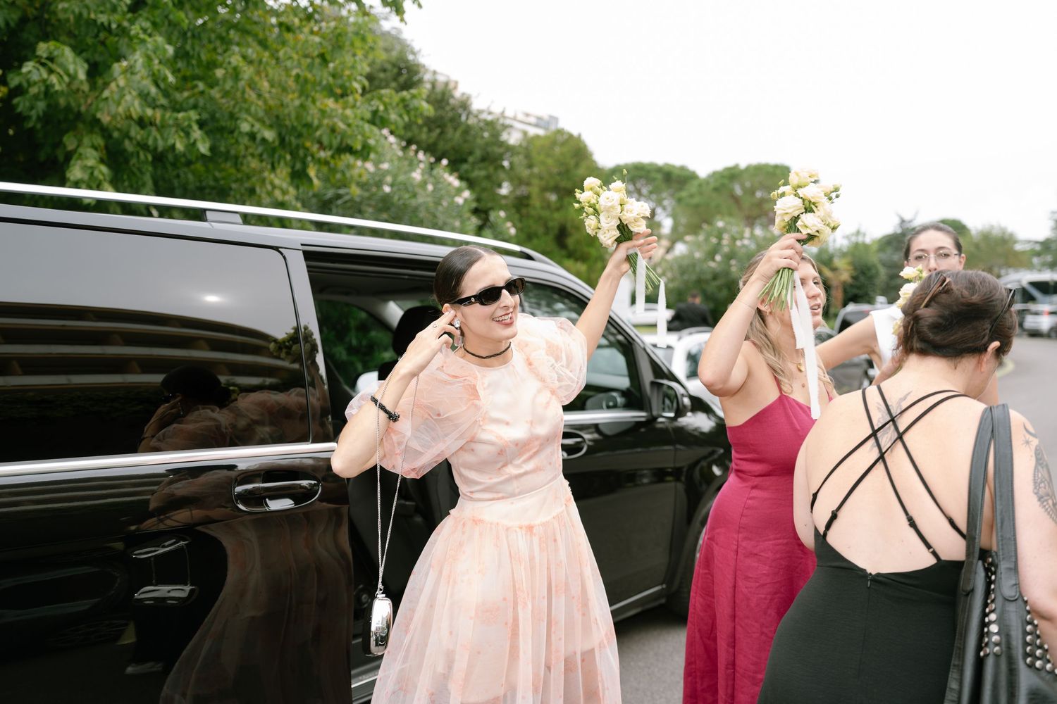 Outdoor wedding scene with people gathering near a black car.