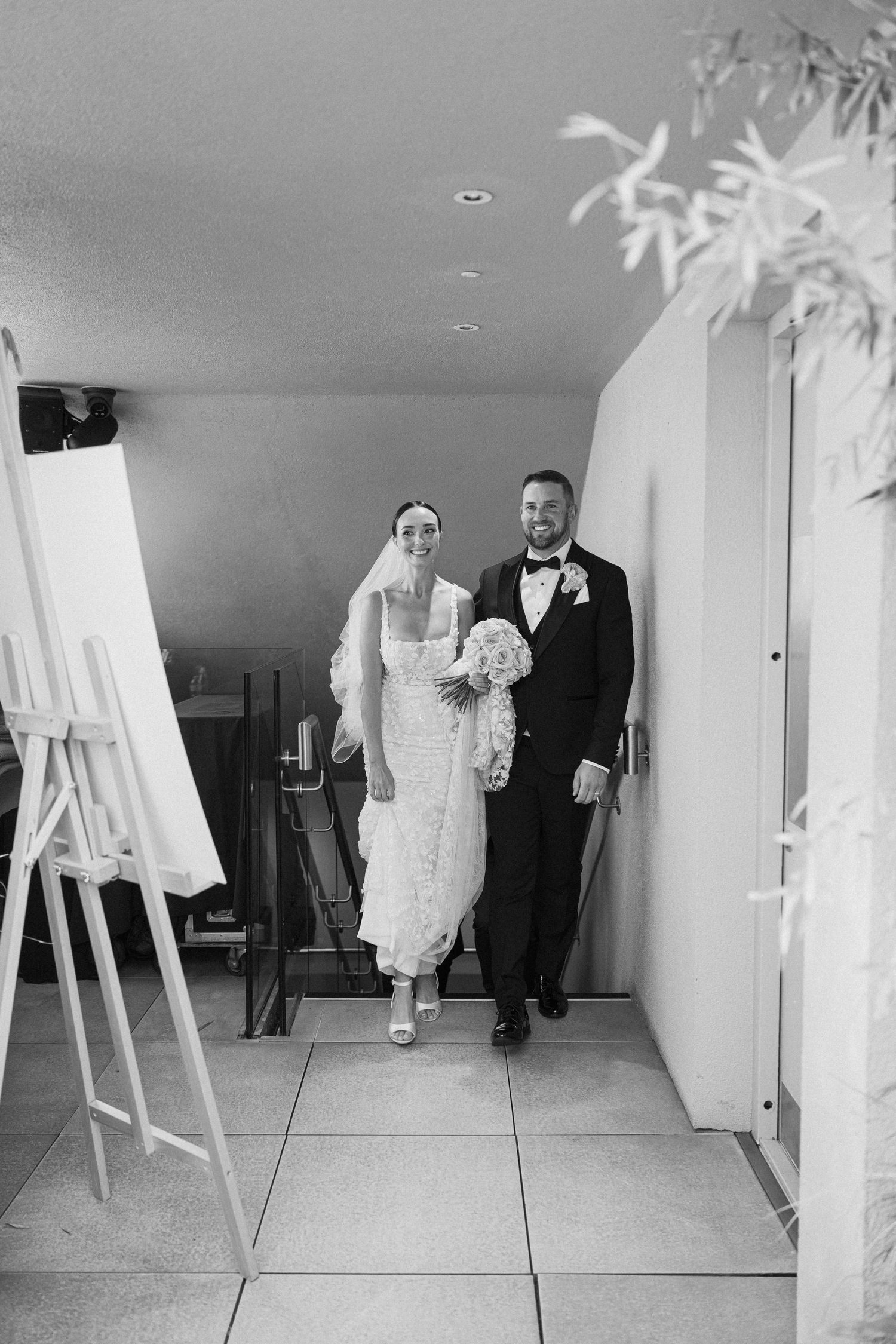 A black and white photo of newlyweds walking down a hallway together.