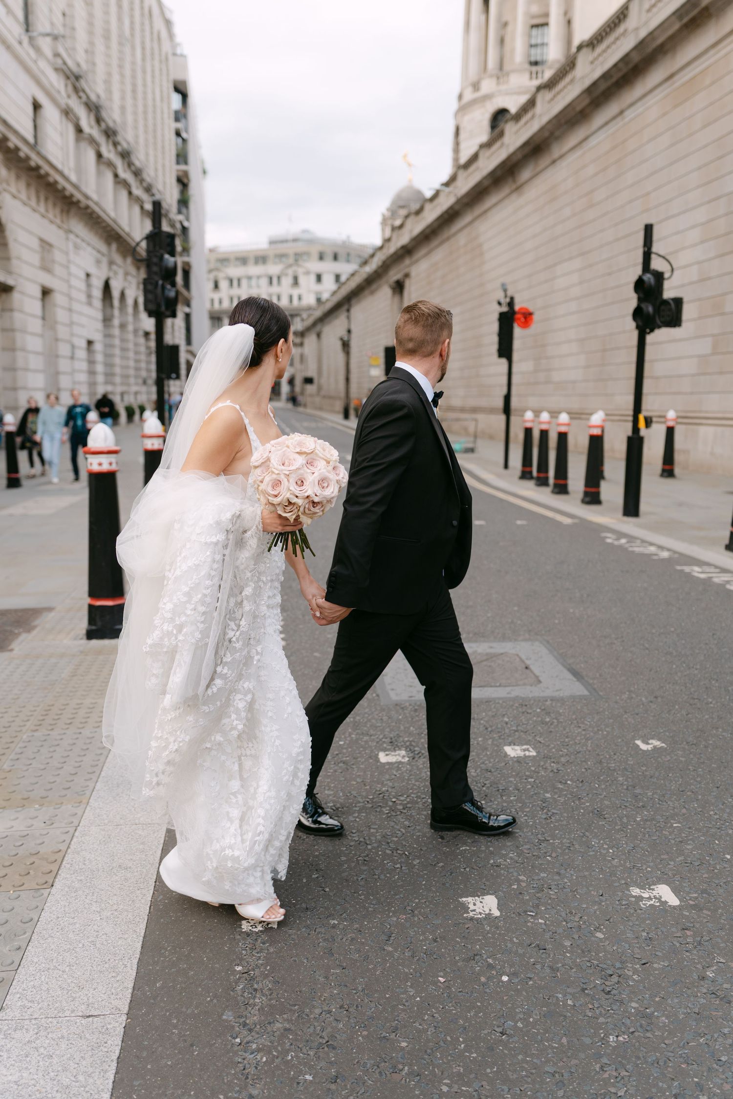 Bride and groom walking down a London street with historic buildings in the background.