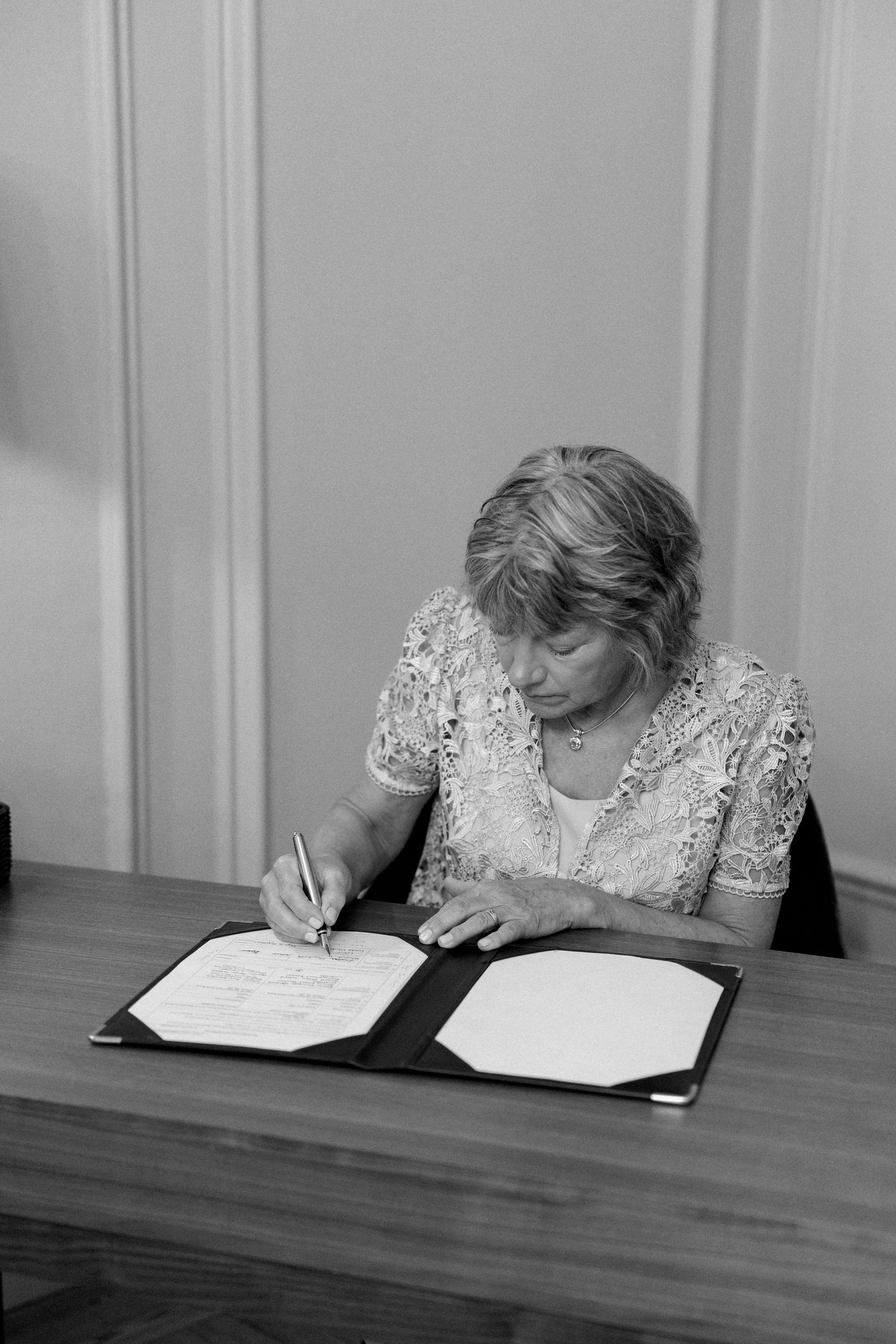 A person in formal attire signing official documents at a wooden table during a ceremony.