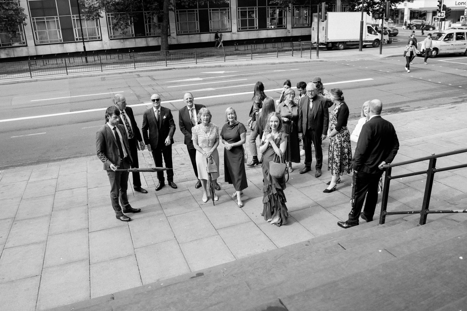 A wedding party gathered outside on a city sidewalk in black and white.