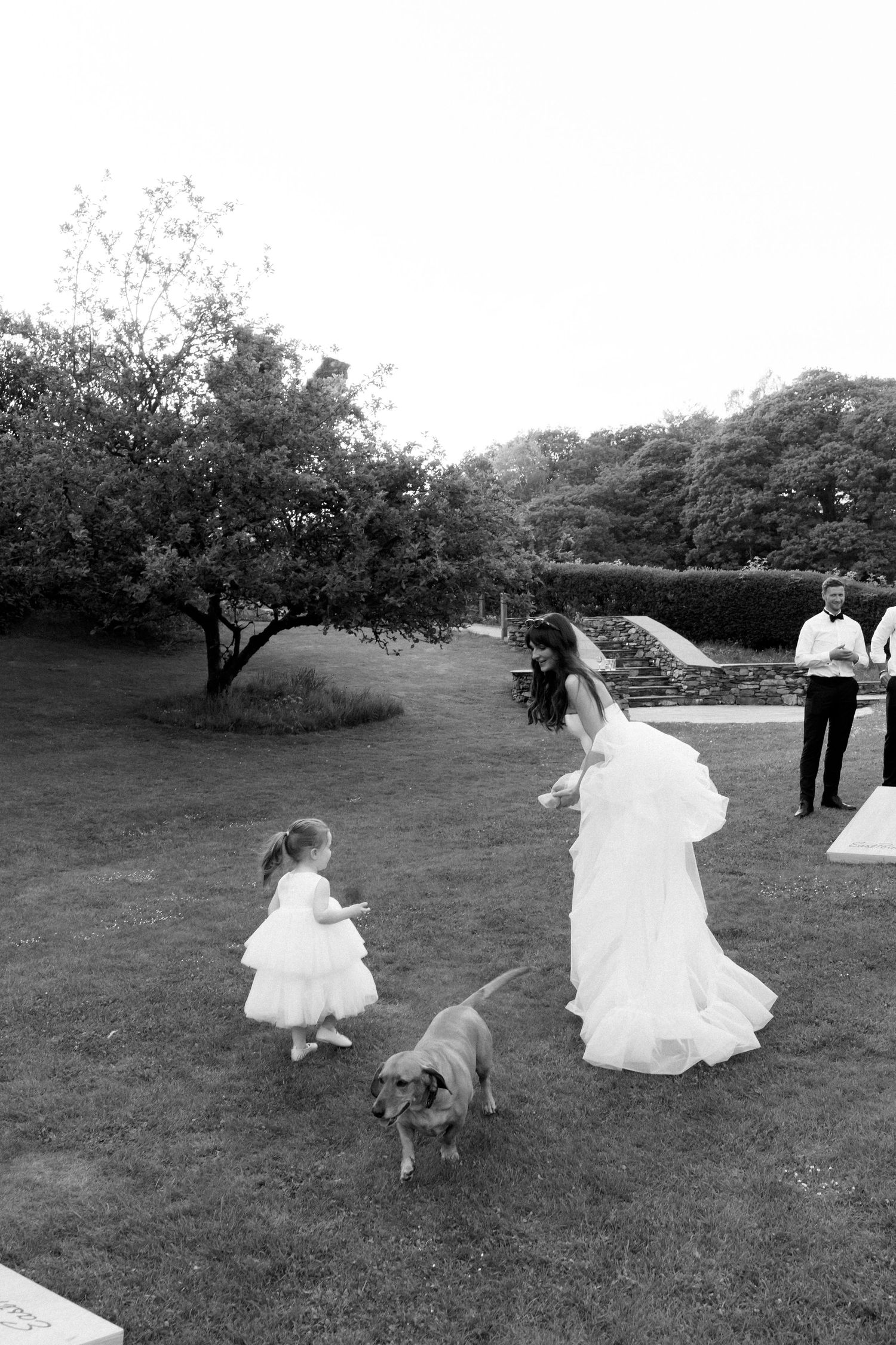 Wedding party members playfully pose and dance on a grassy lawn.