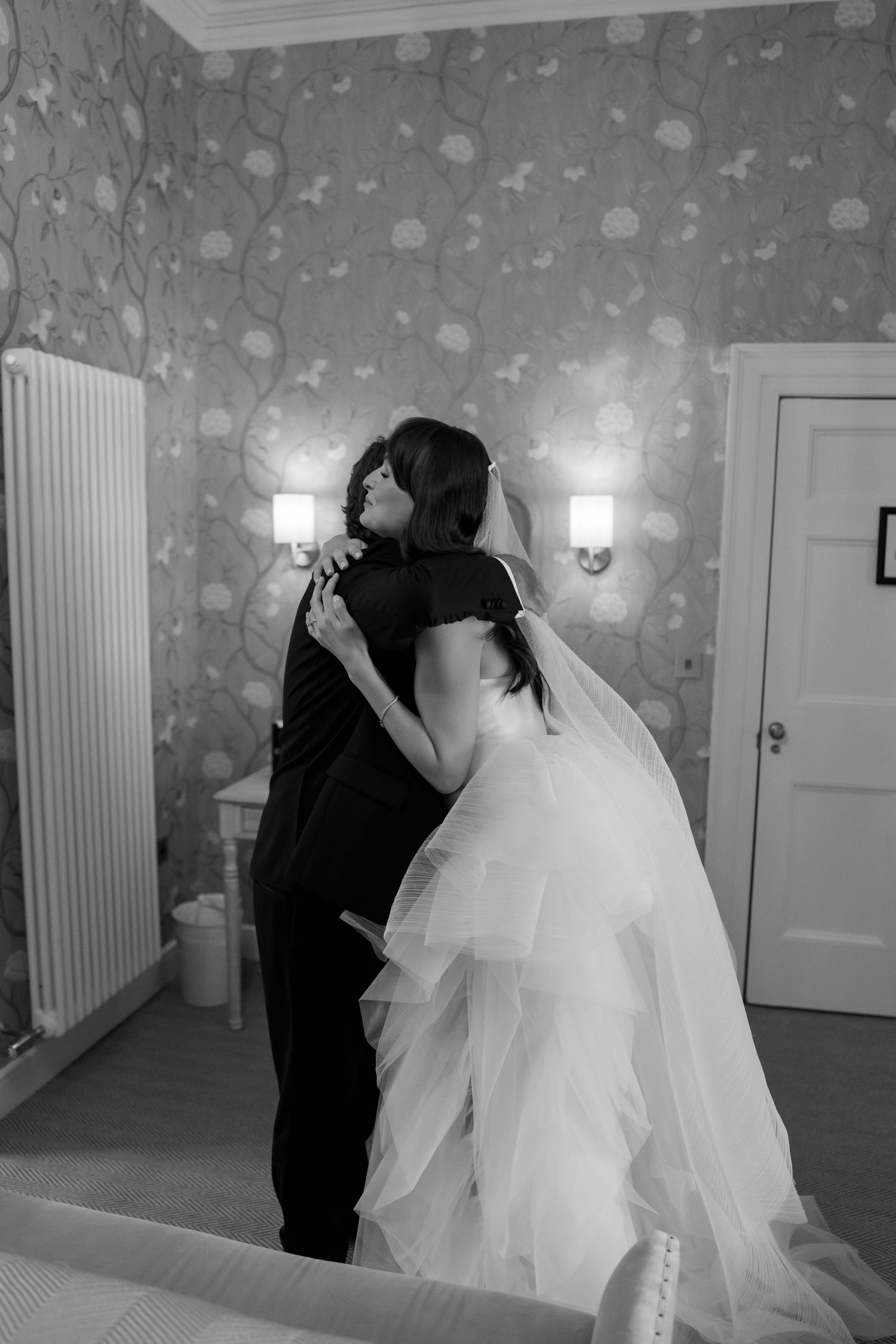 An emotional black and white wedding moment capturing an embrace in a beautifully decorated room.