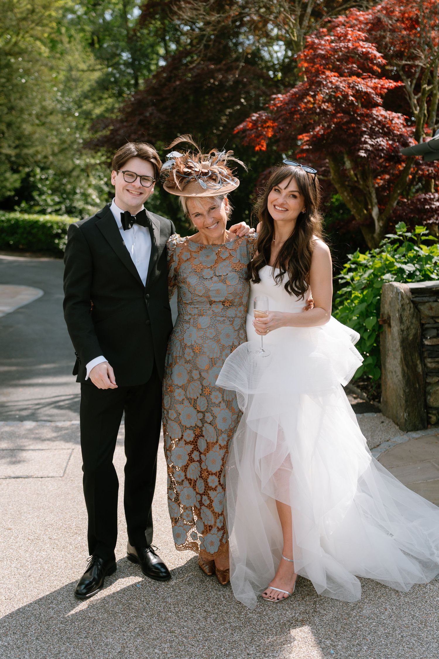 Wedding couple poses for portraits in a garden with blooming red maple trees.