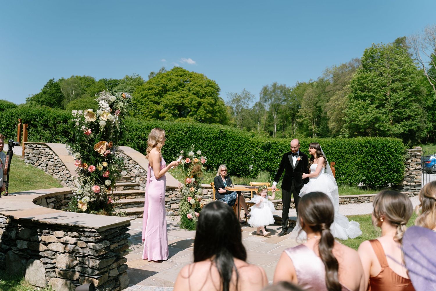 Wedding celebration on an outdoor stone patio with pink-dressed attendants and decorative flowers.