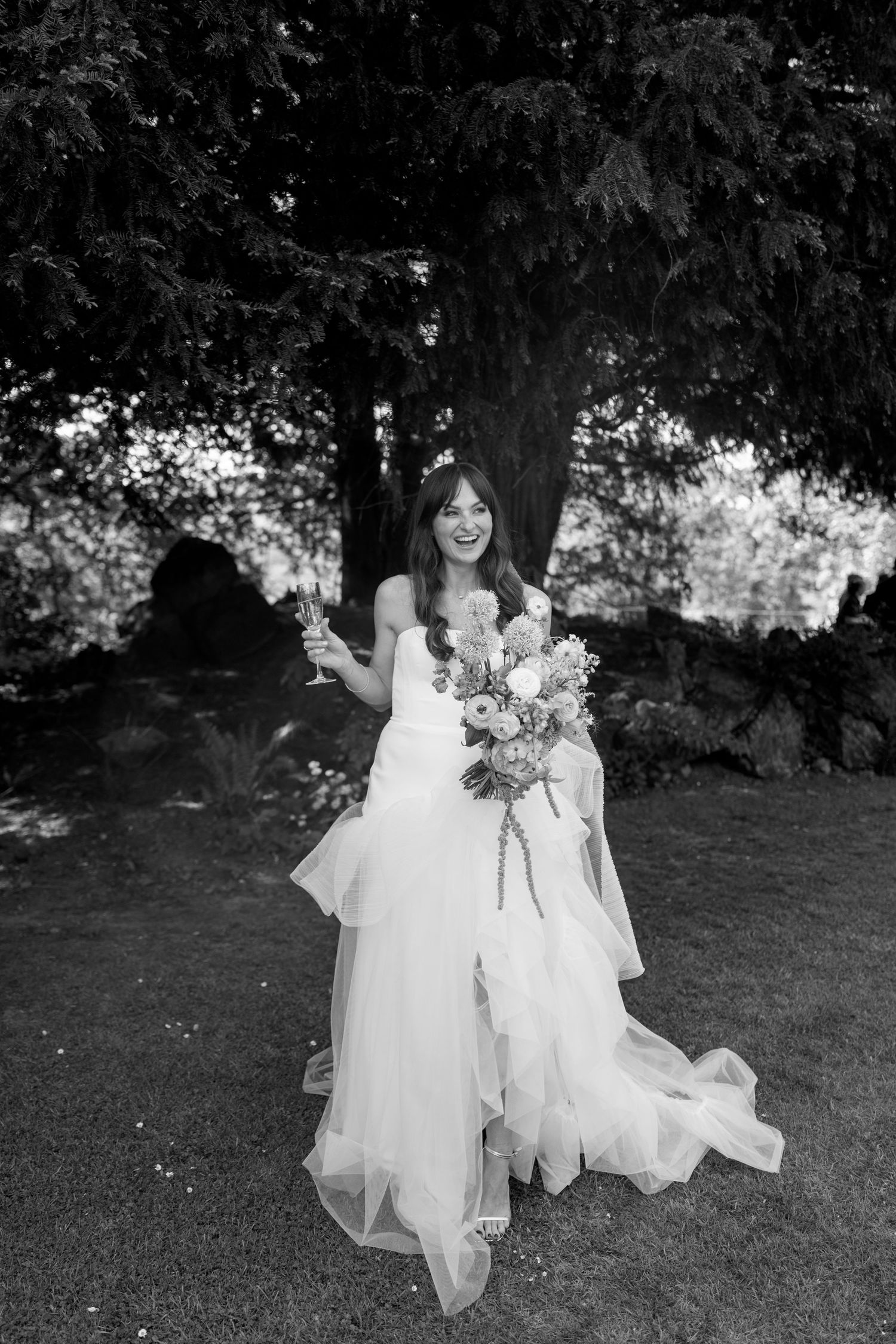 Black and white photo of elegant wedding dresses flowing across garden lawn.