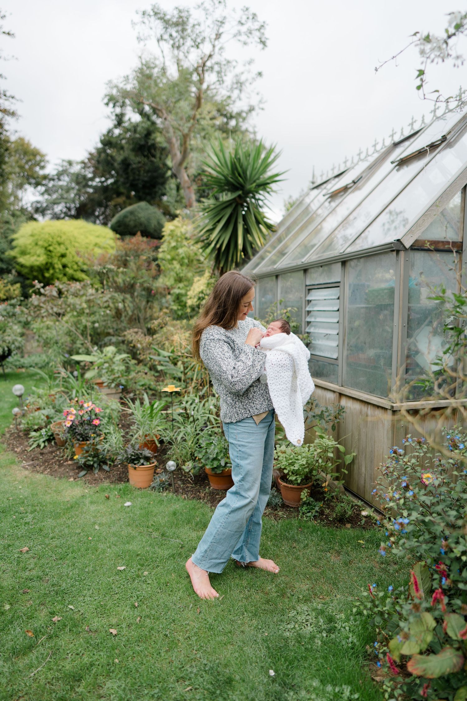 Person in denim overalls exploring a garden with greenhouse in background.