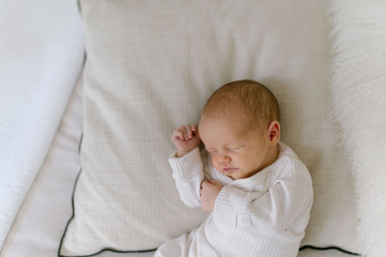 Sleeping baby in white clothing nestled in soft bedding.