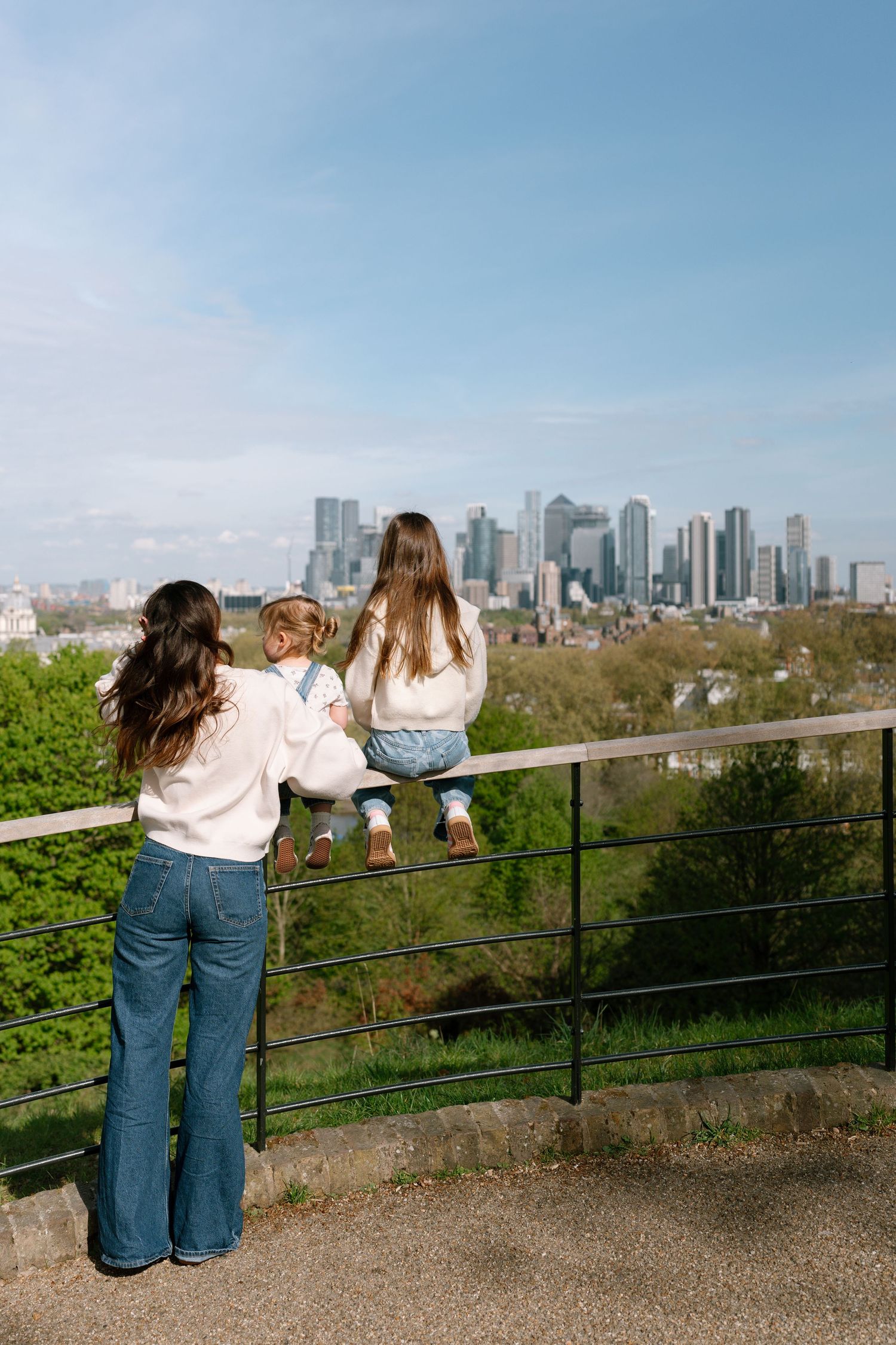 Three people lean on a railing overlooking a city skyline on a sunny day.