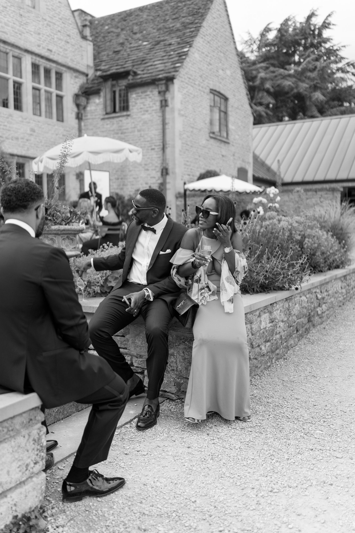 Black and white photo of elegantly dressed wedding guests socializing outdoors at a countryside manor estate.