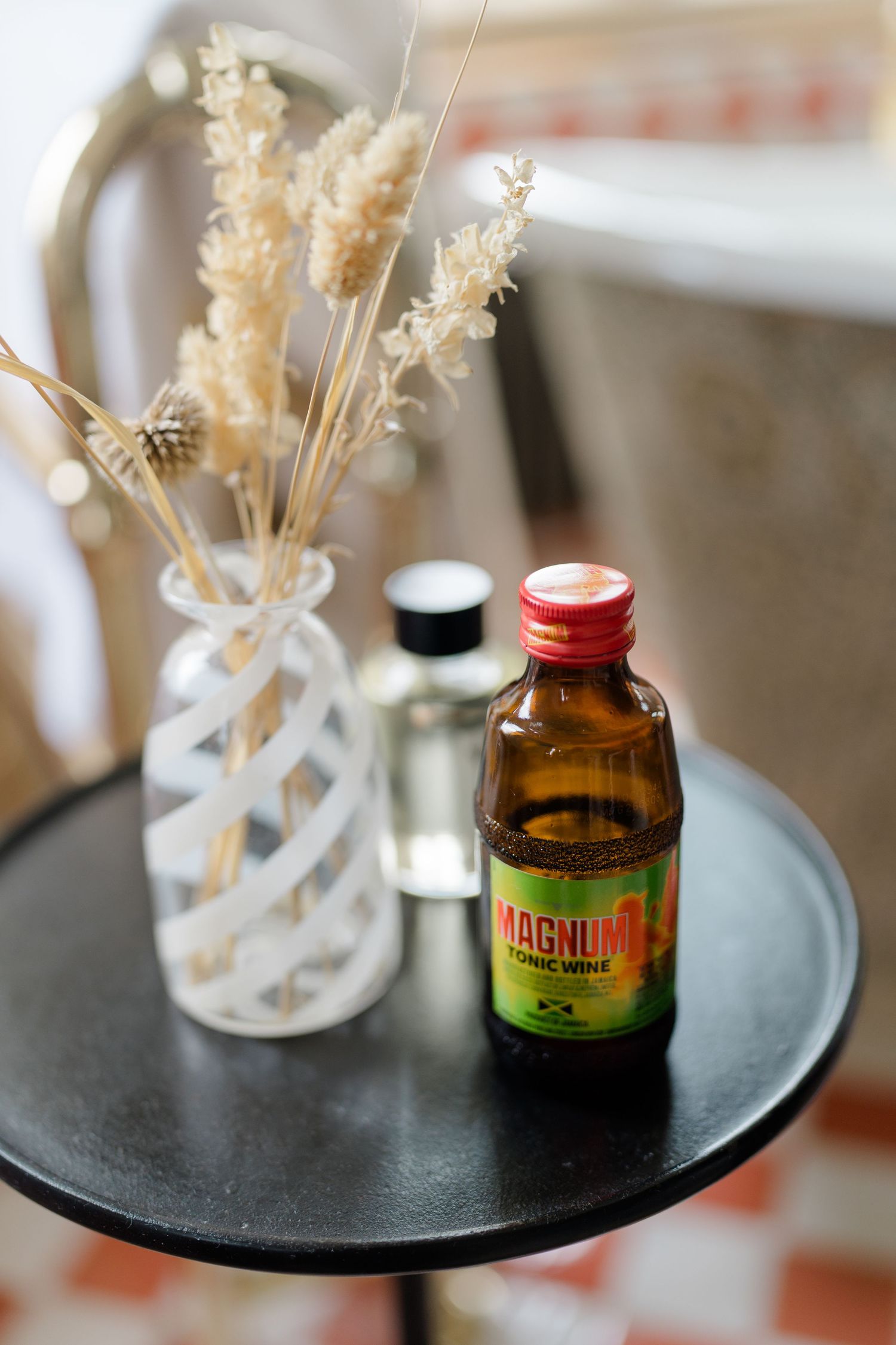Magnum tonic wine bottle on black side table with dried flower arrangement in white vase.