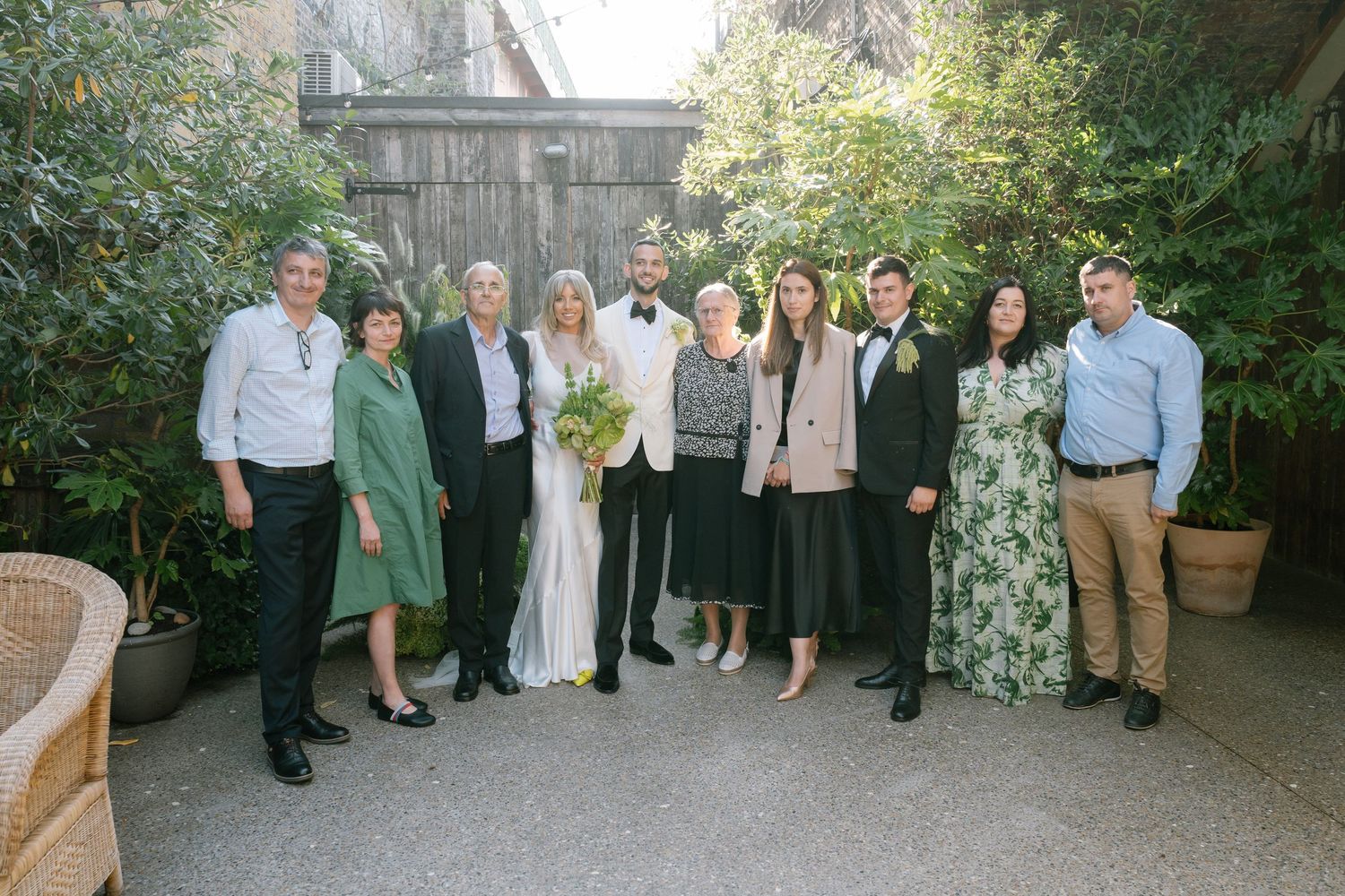 Wedding party poses for a formal group photo in an outdoor garden setting.