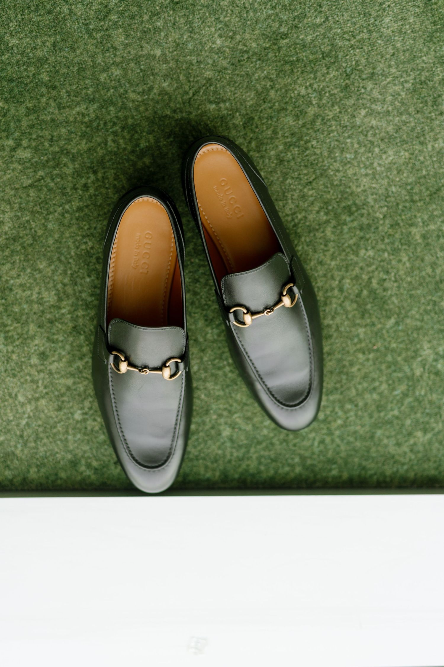Gray leather Gucci loafers with gold hardware photographed on green carpet.