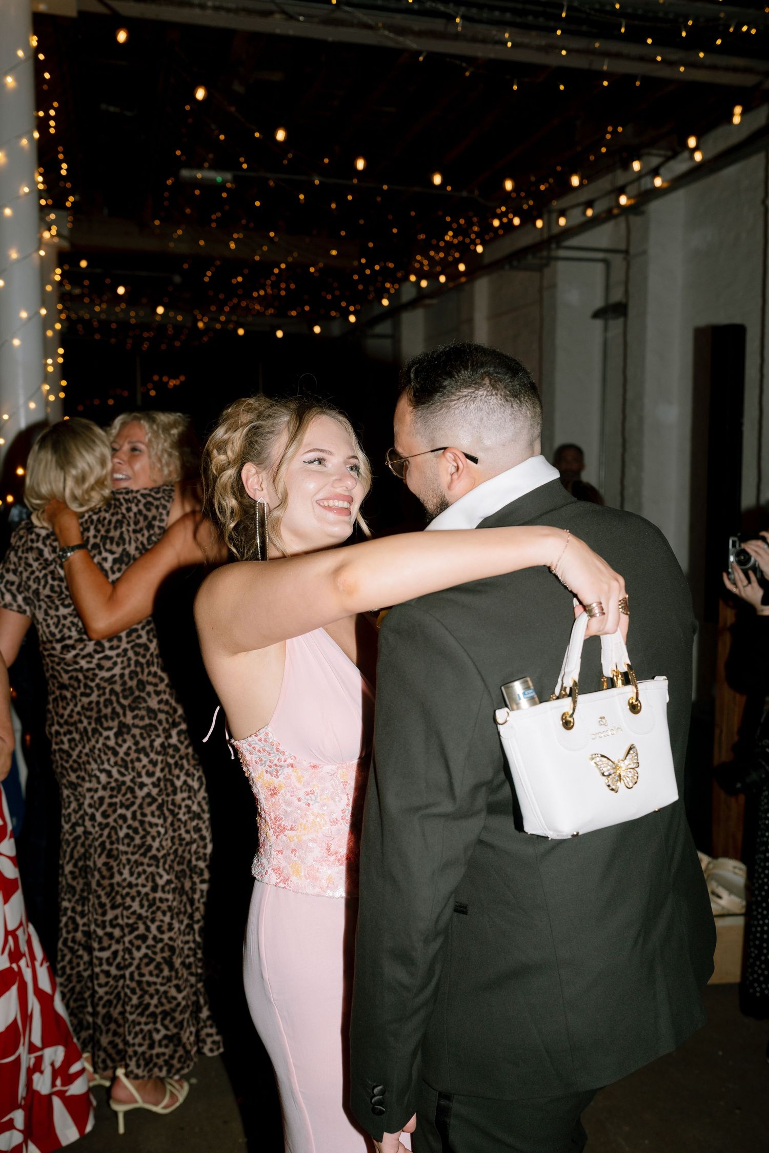 Wedding reception dance floor with string lights overhead and guests in formal attire.