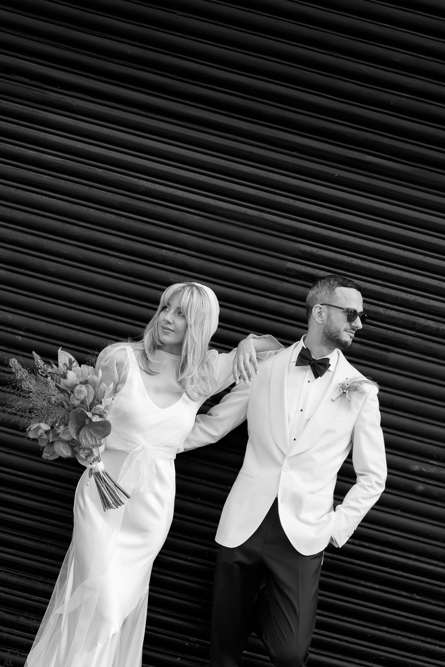 Artistic black and white wedding portrait against industrial metal backdrop with dramatic poses.