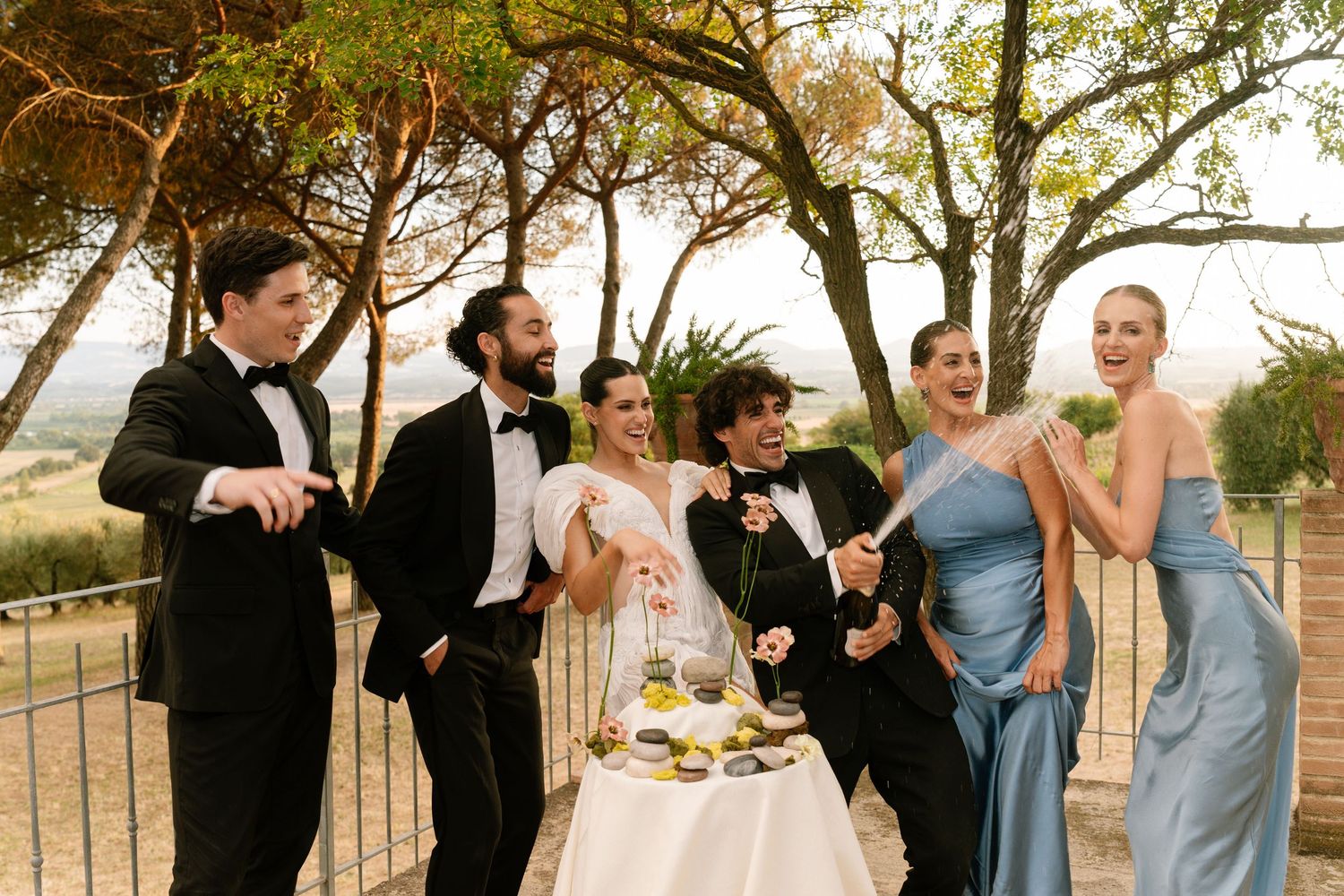 Wedding party celebrating outdoors with joyful expressions and formal attire.