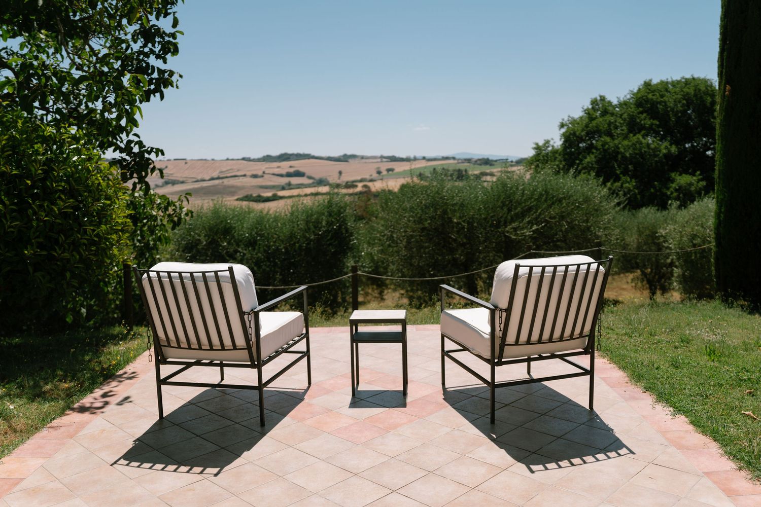 Two modern outdoor lounge chairs sit on a paved terrace overlooking a scenic countryside landscape.