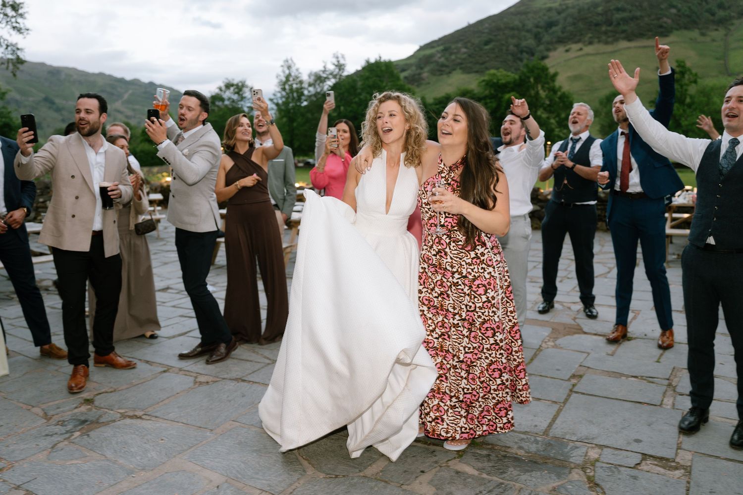 Wedding guests dancing and celebrating outdoors with mountain landscape in background.
