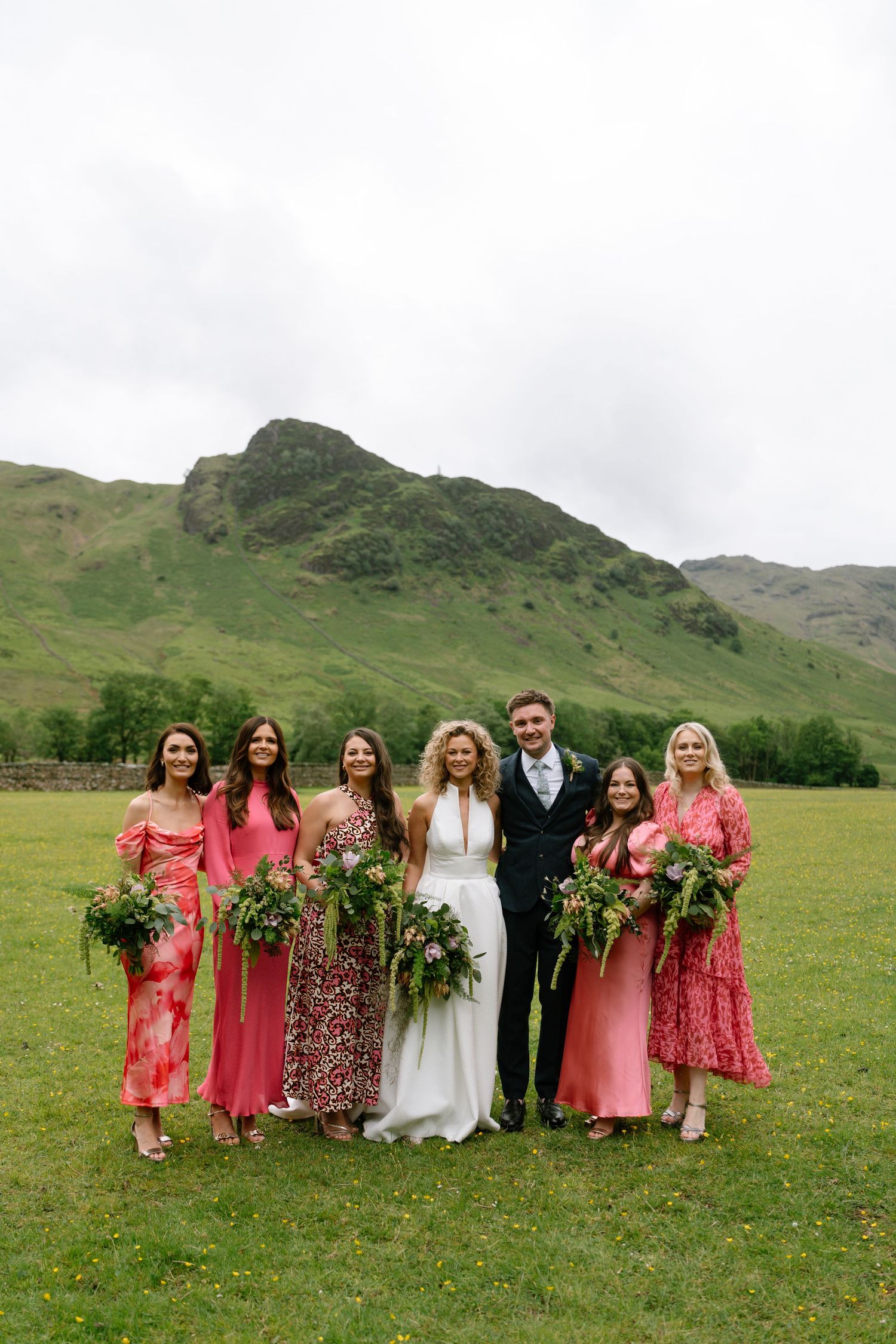 Wedding party in pink dresses poses against dramatic mountain landscape.