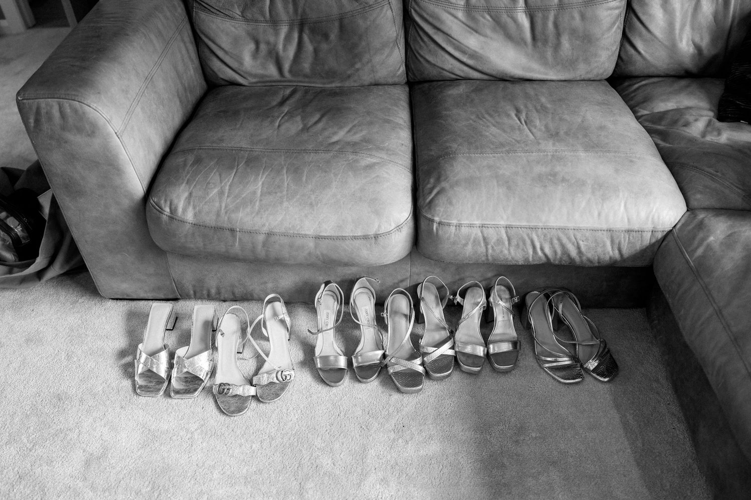 Multiple pairs of white and silver bridal shoes lined up in a row on a gray couch.