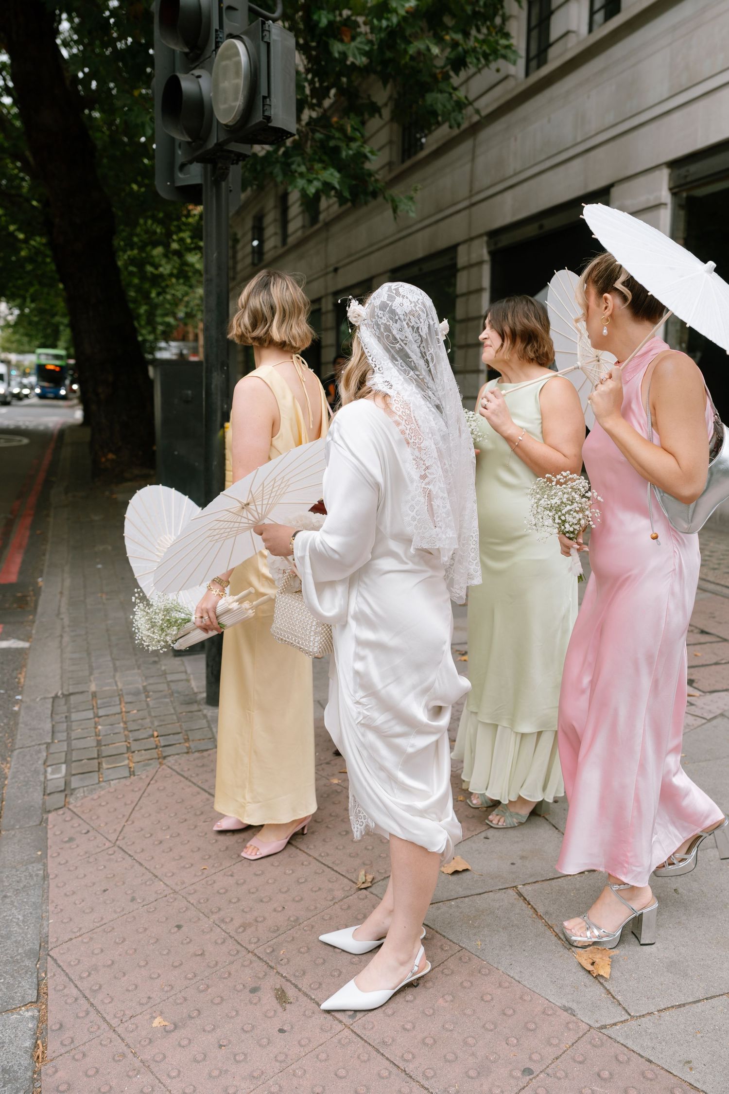 Wedding party in white and pink dresses walking along a cobblestone sidewalk.