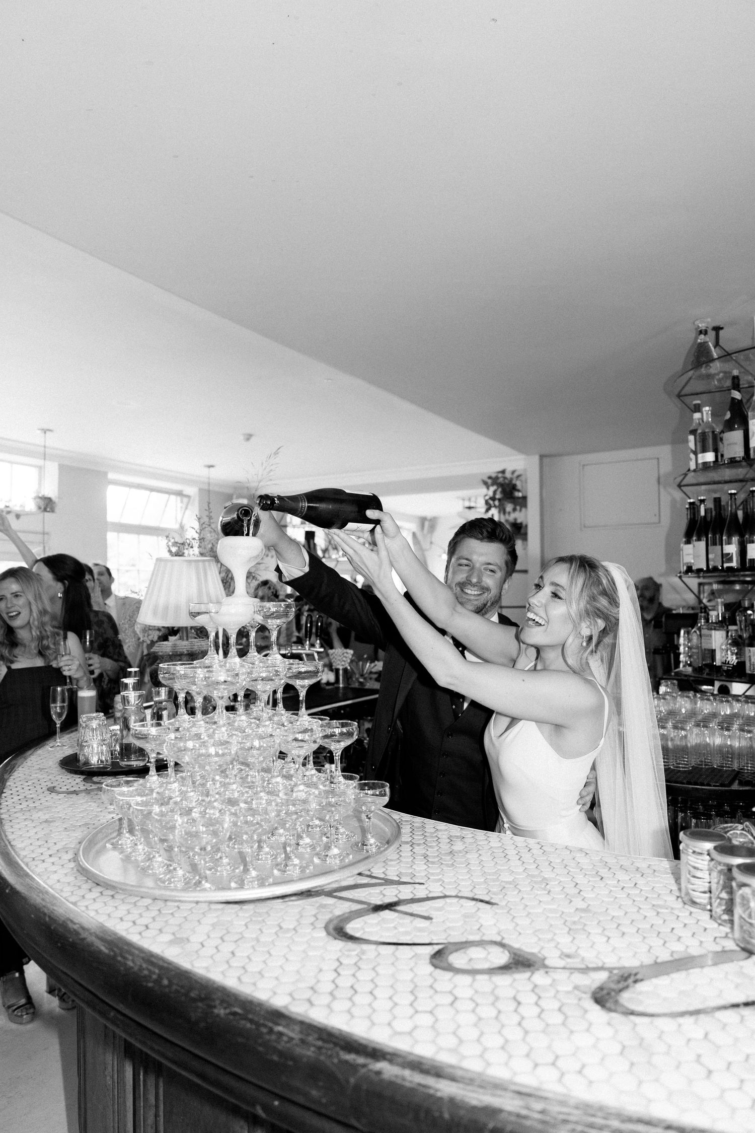 Pouring champagne into tower of glasses at elegant bar celebration.