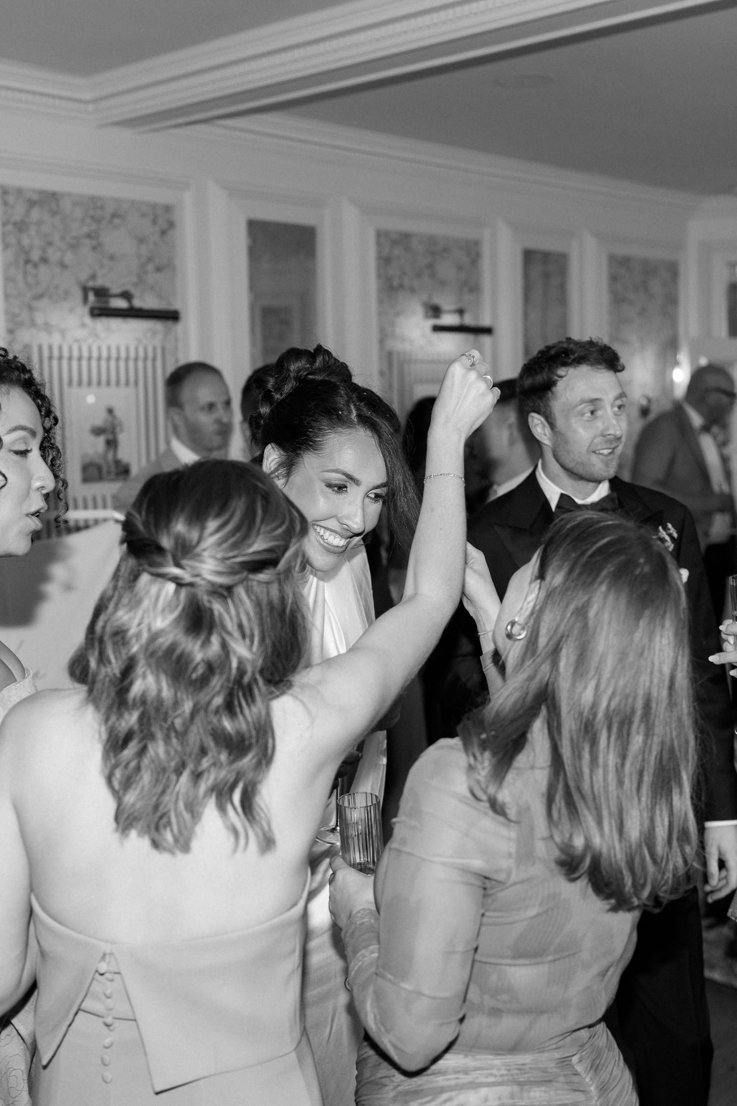 Bride laughing and dancing joyfully with guests during a lively indoor wedding reception celebration.