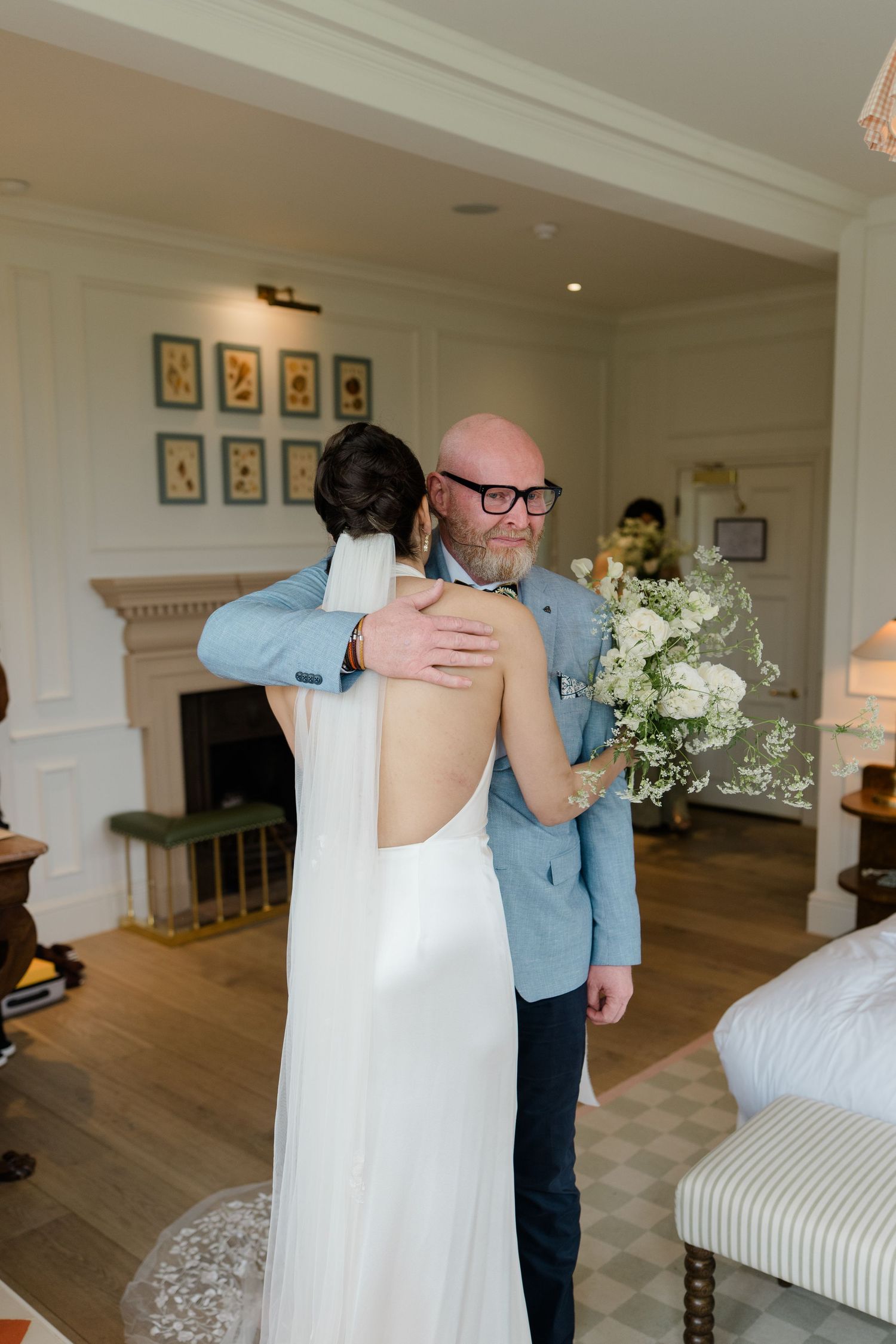 Emotional father hugs bride in backless white wedding dress during first look moment.