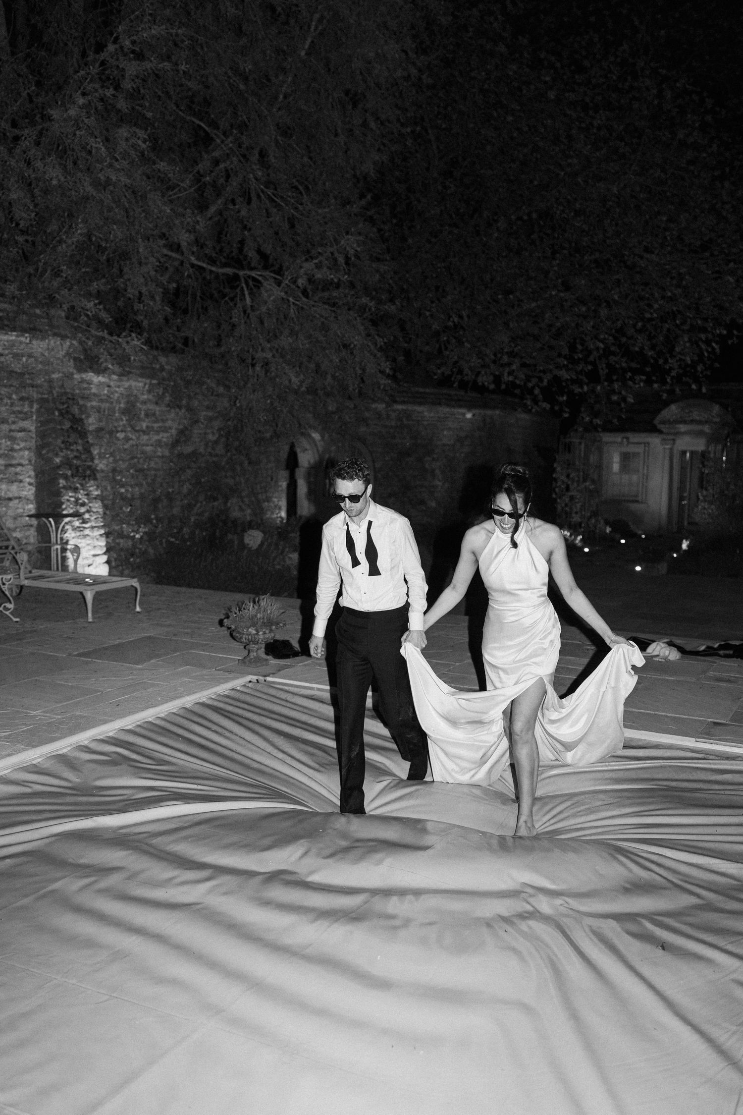 Black and white photo of bride and groom walking hand in hand outdoors at night.