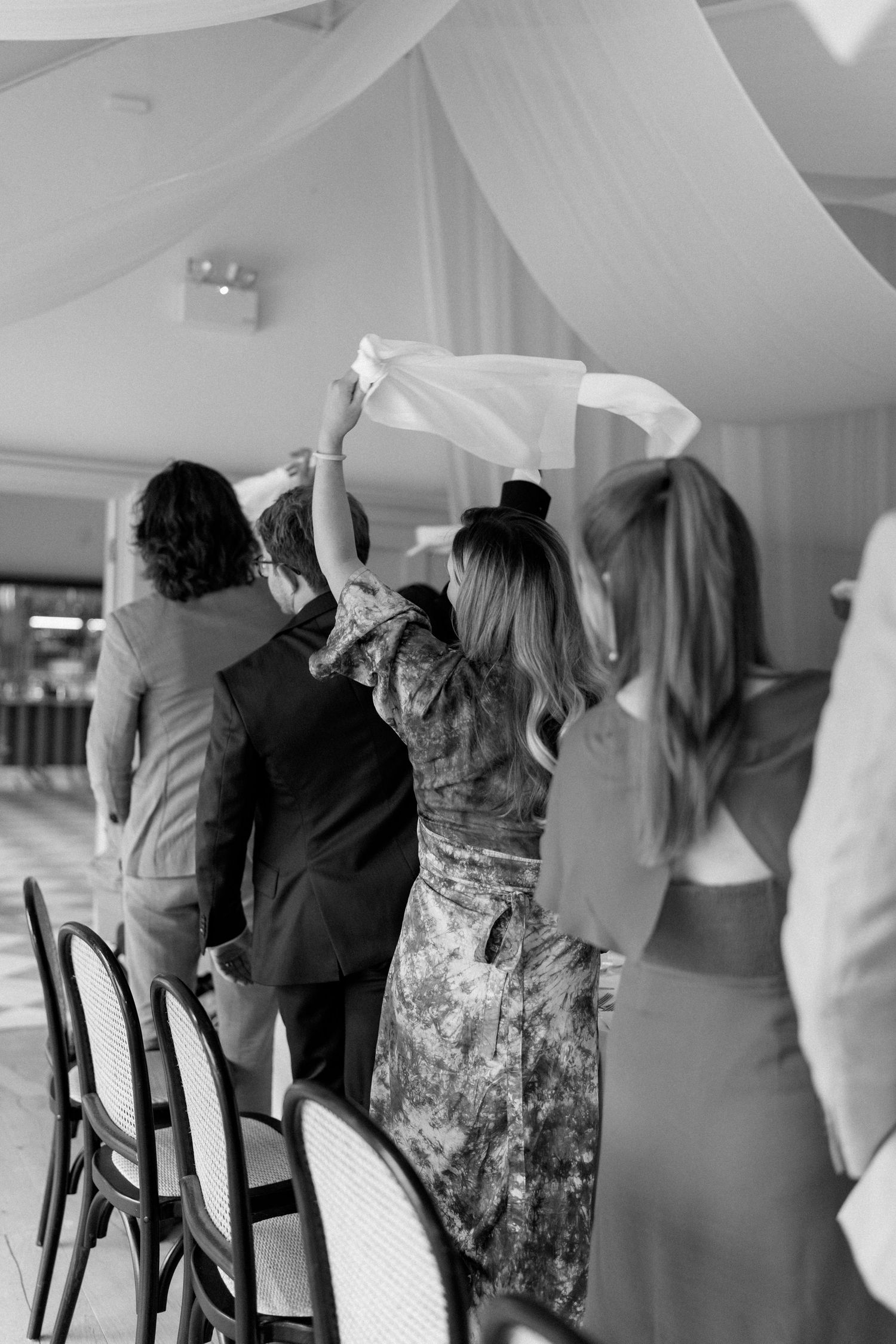 Wedding guests waving napkins in celebration inside draped marquee reception venue.