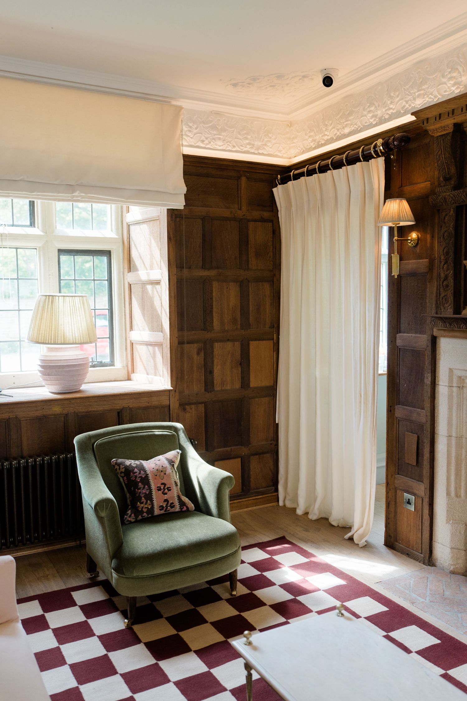 Elegant manor house interior with green velvet armchair and burgundy checkered floor rug.