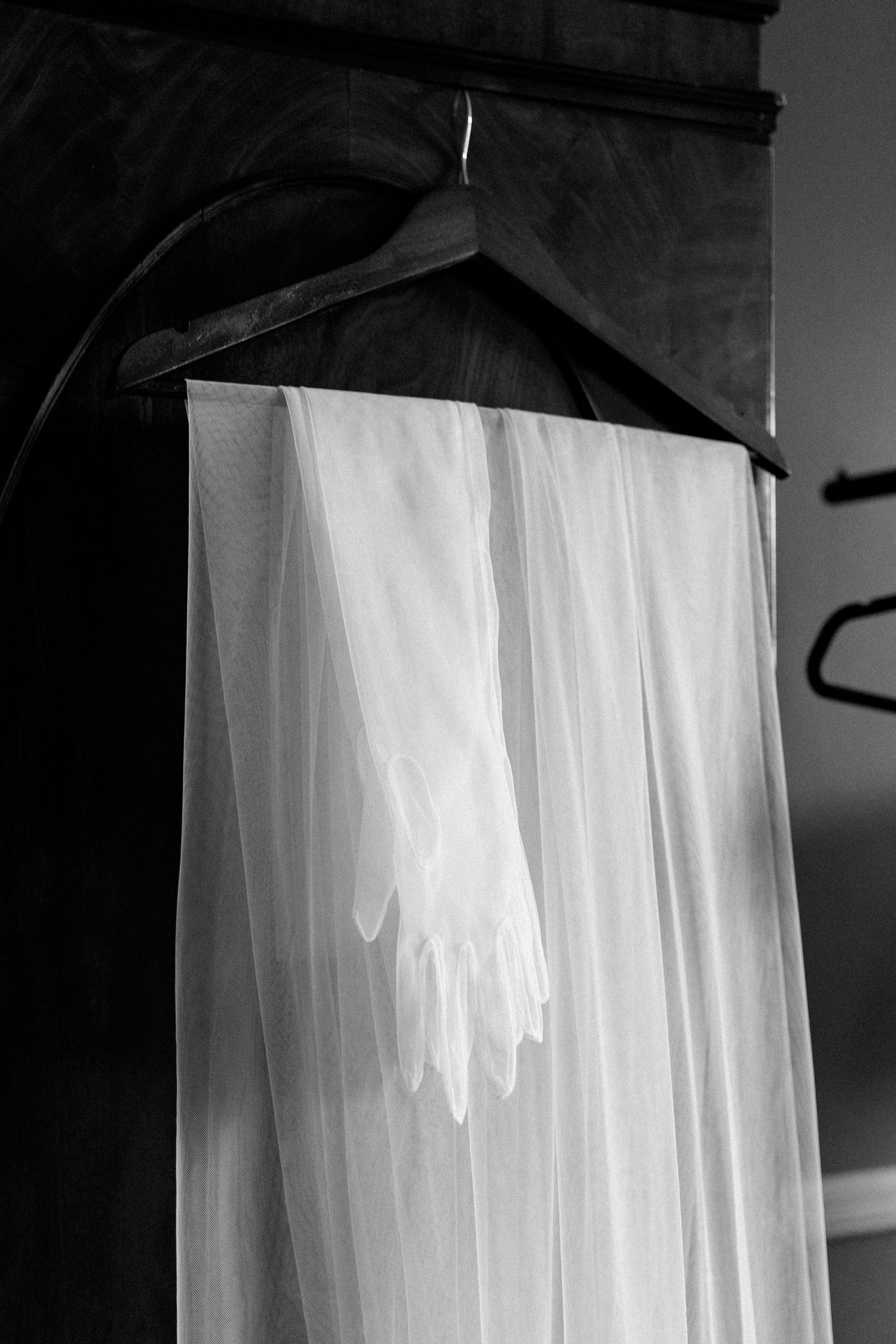 A white wedding veil and gloves hanging on a wooden hanger in black and white.