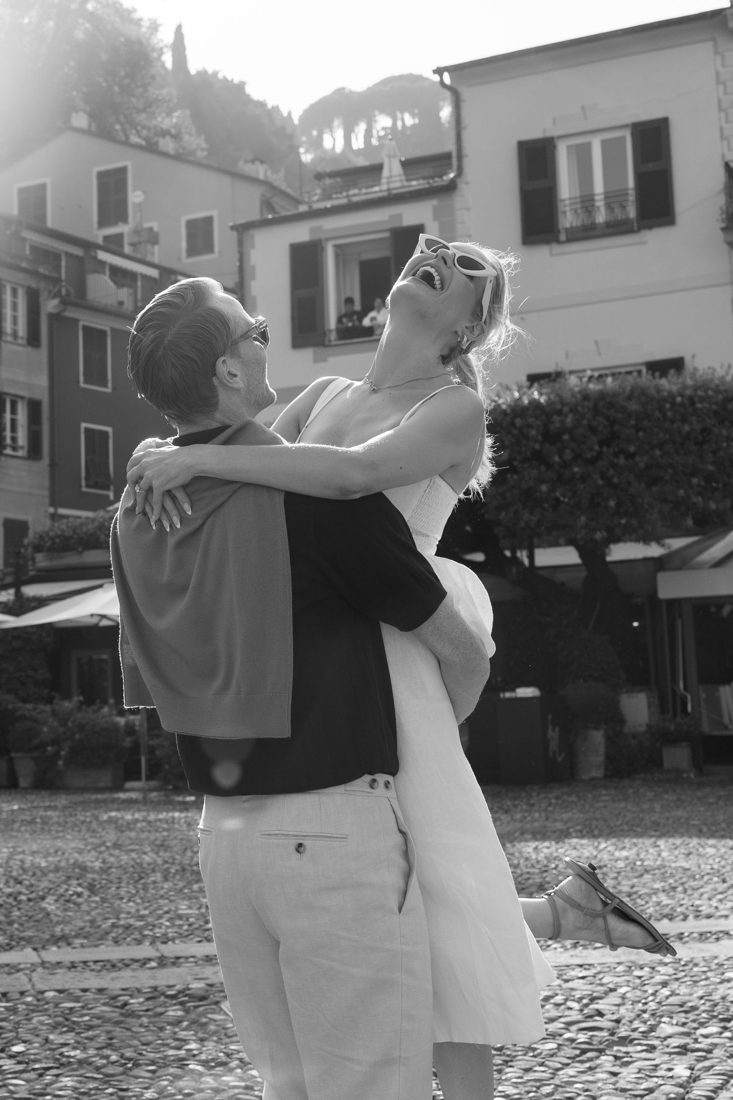 Black and white photo of a joyful couple embracing and laughing in a European cobblestone square.