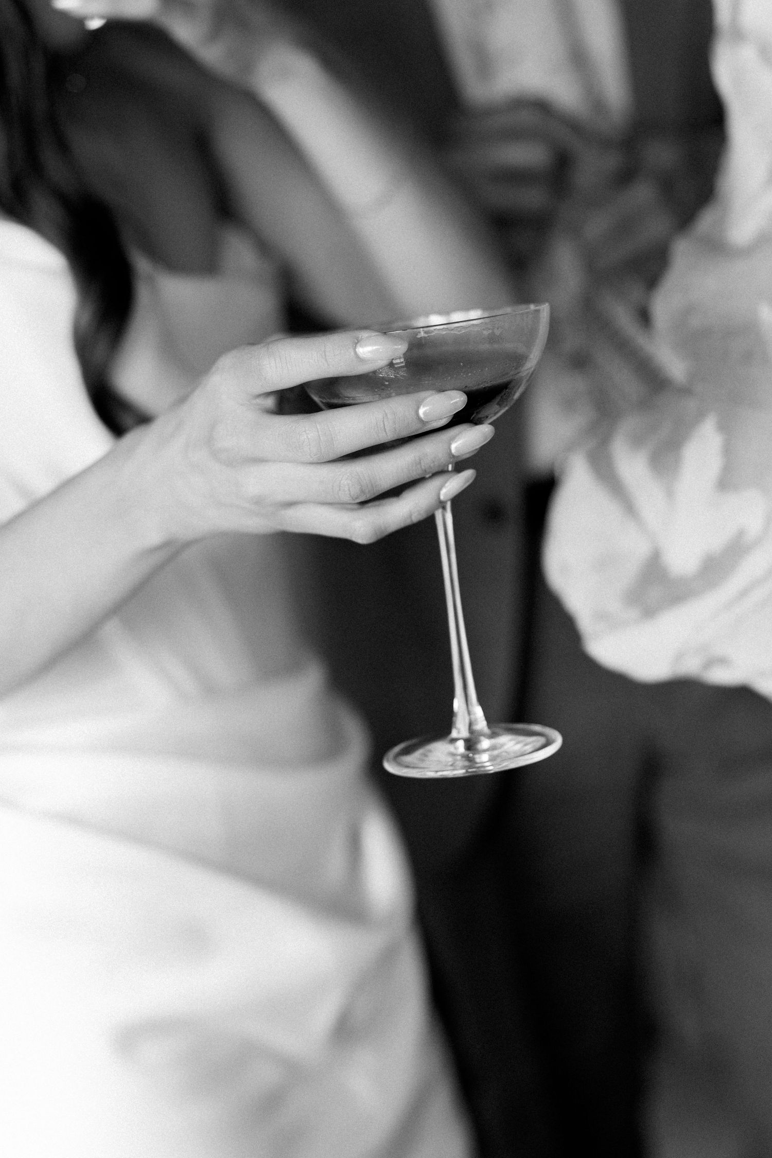 Black and white close-up of bride holding a coupe cocktail glass at wedding reception.