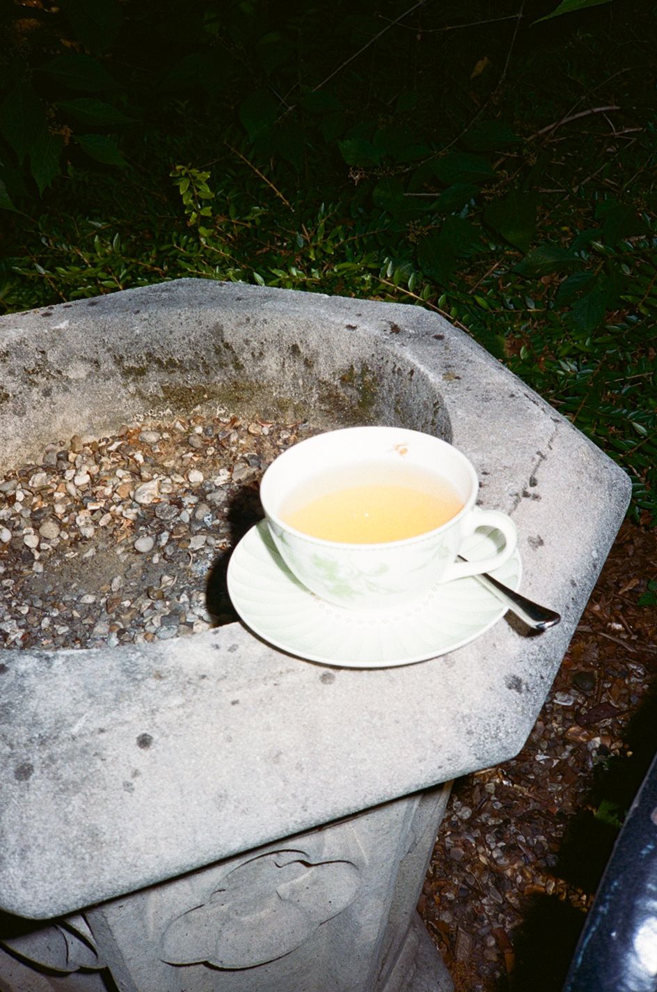A white teacup with green tea on a saucer, resting on a weathered stone planter outdoors.