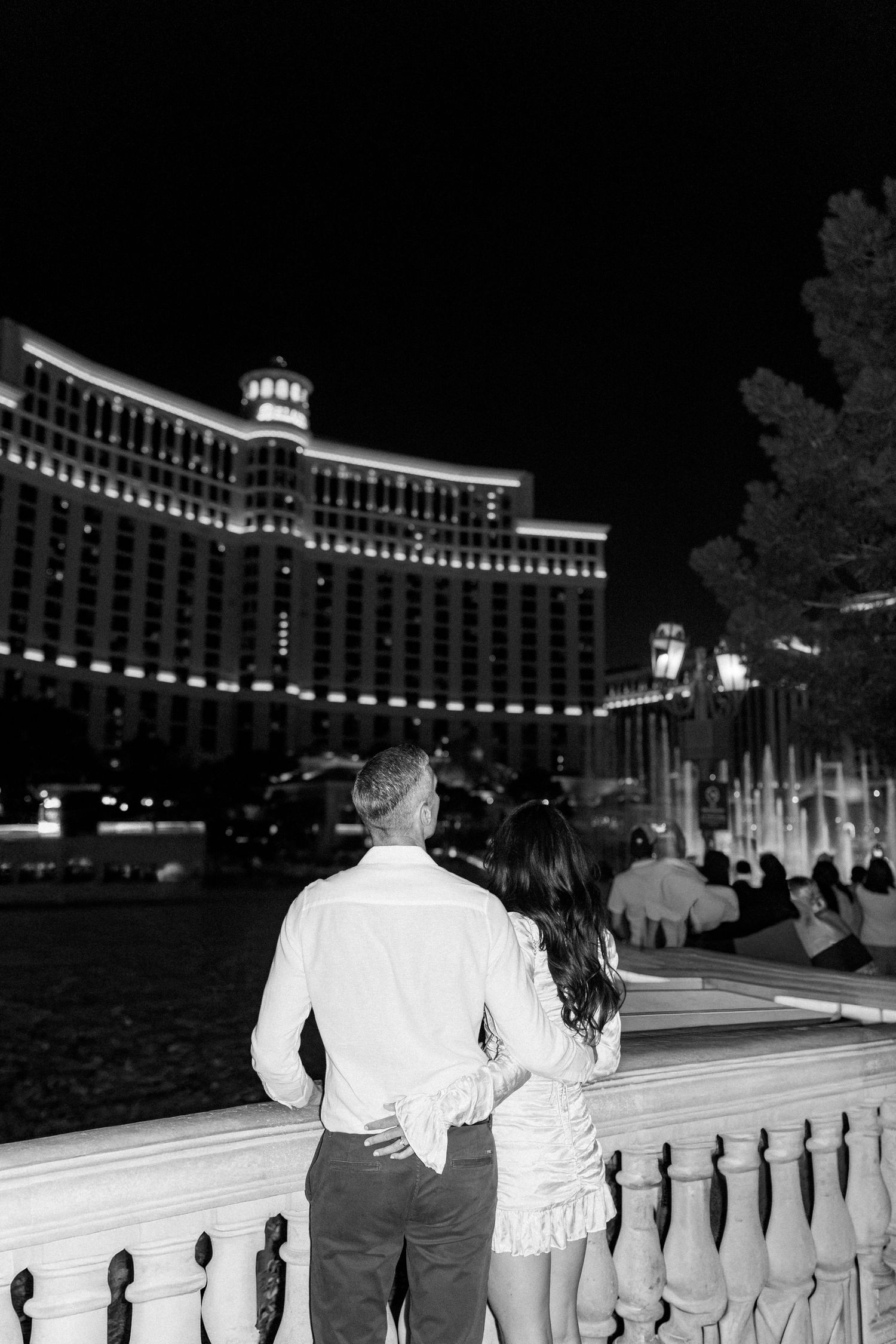 A couple admires the illuminated Bellagio hotel from a balcony overlooking the fountains.