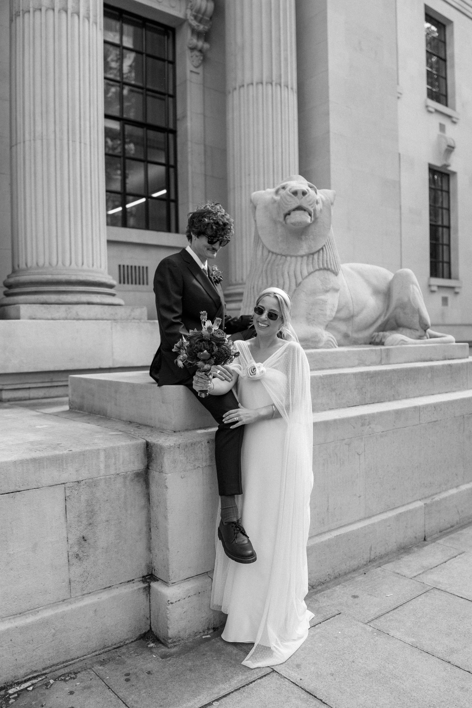 Wedding couple poses creatively against stone steps and columns of a historic building.