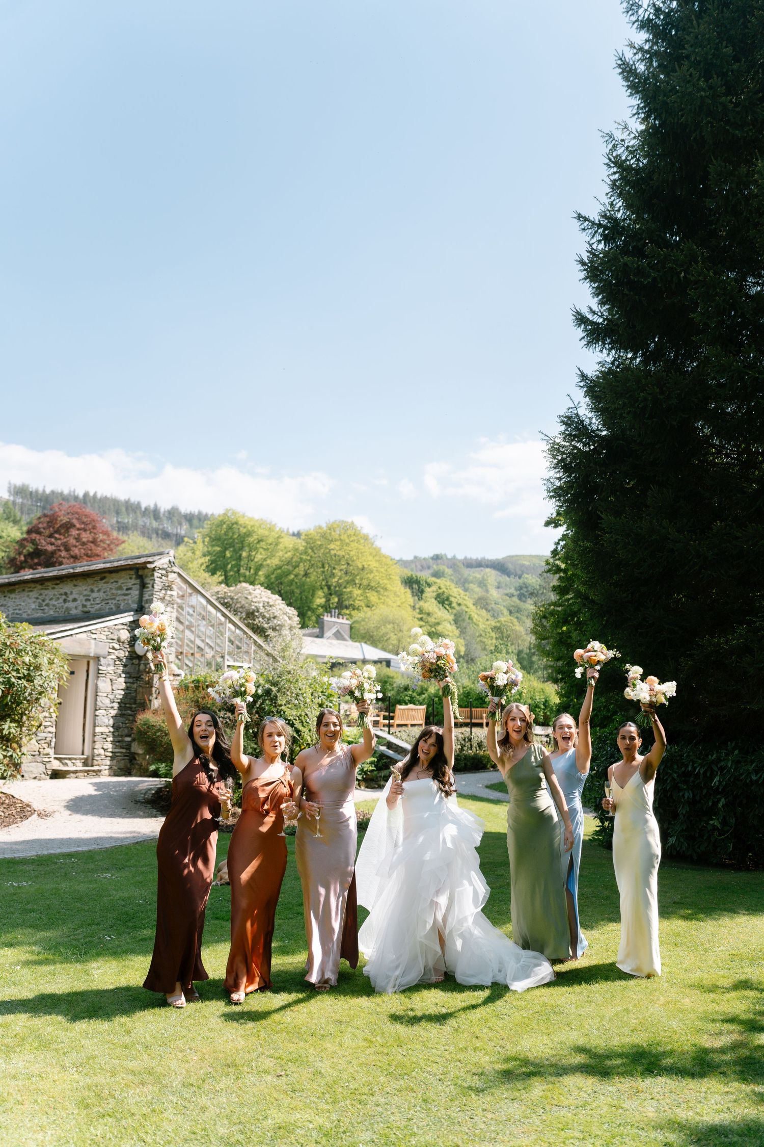 Wedding party celebrates on a lawn with a stone building in the background.