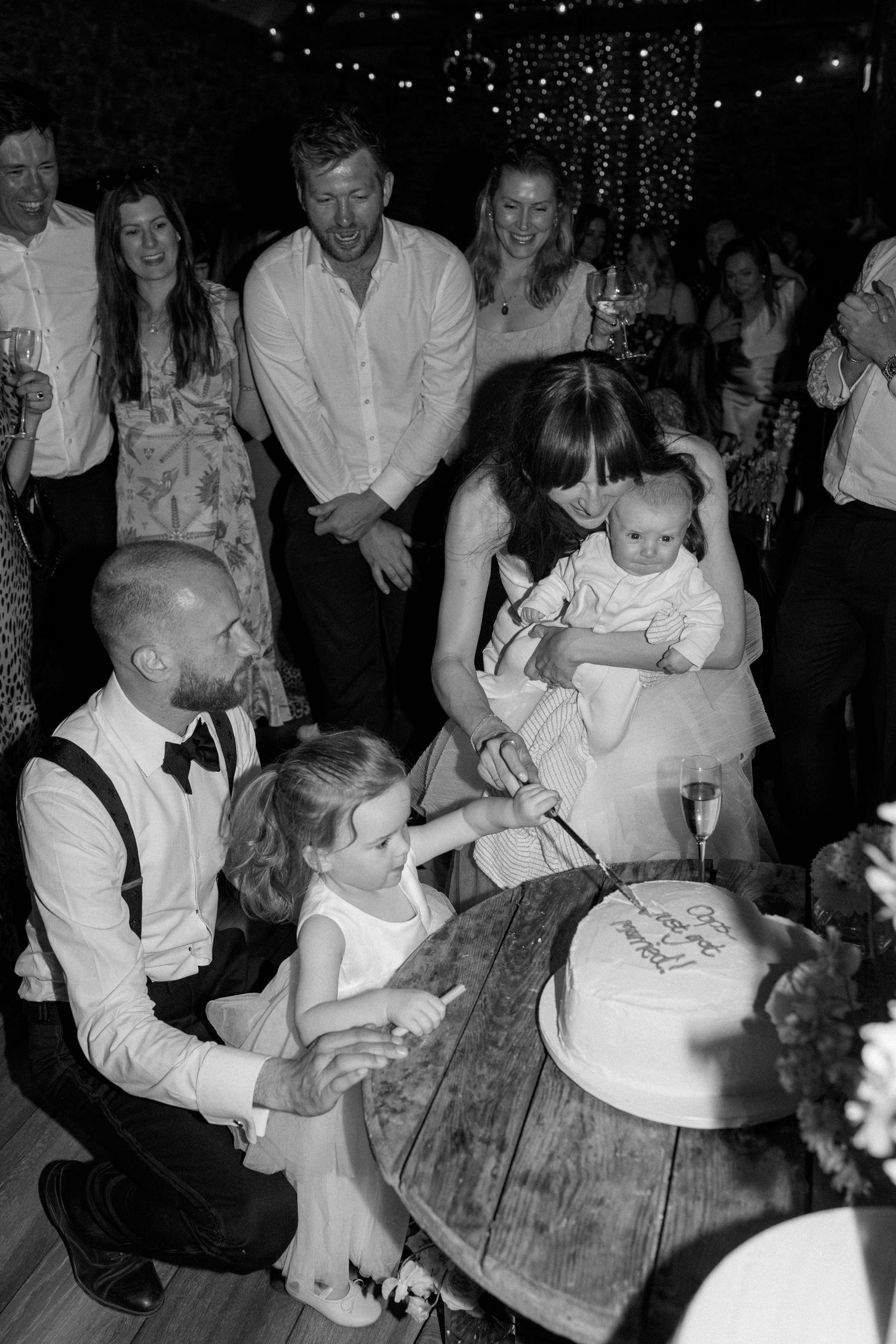 Wedding guests gather around rustic wooden tables during an evening celebration.