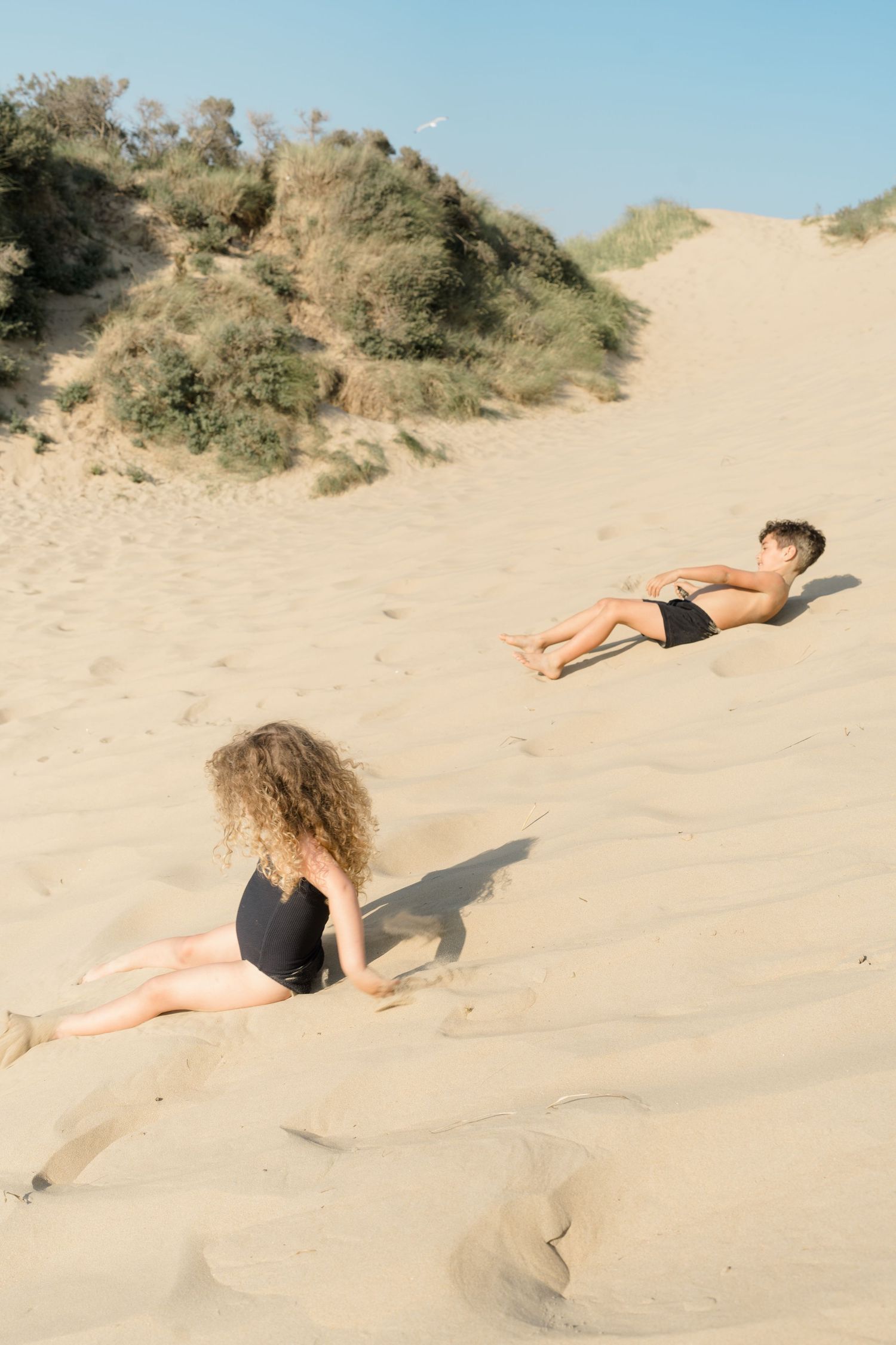 Dancer gracefully poses on sandy beach dunes against blue sky in artistic photo series.