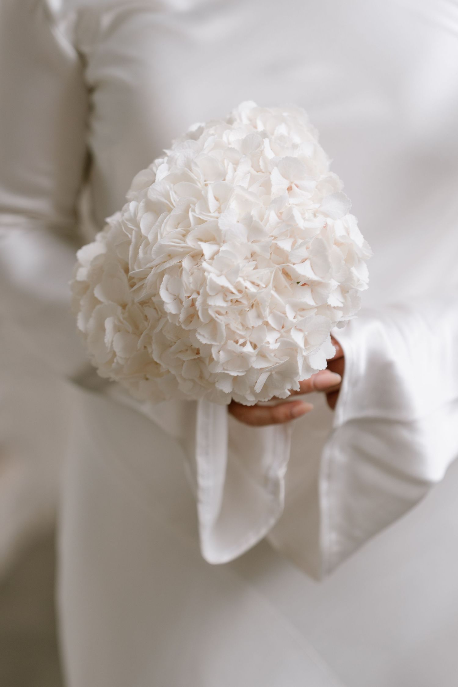 White silk gloves delicately hold a soft white carnation bouquet with ruffled petals.