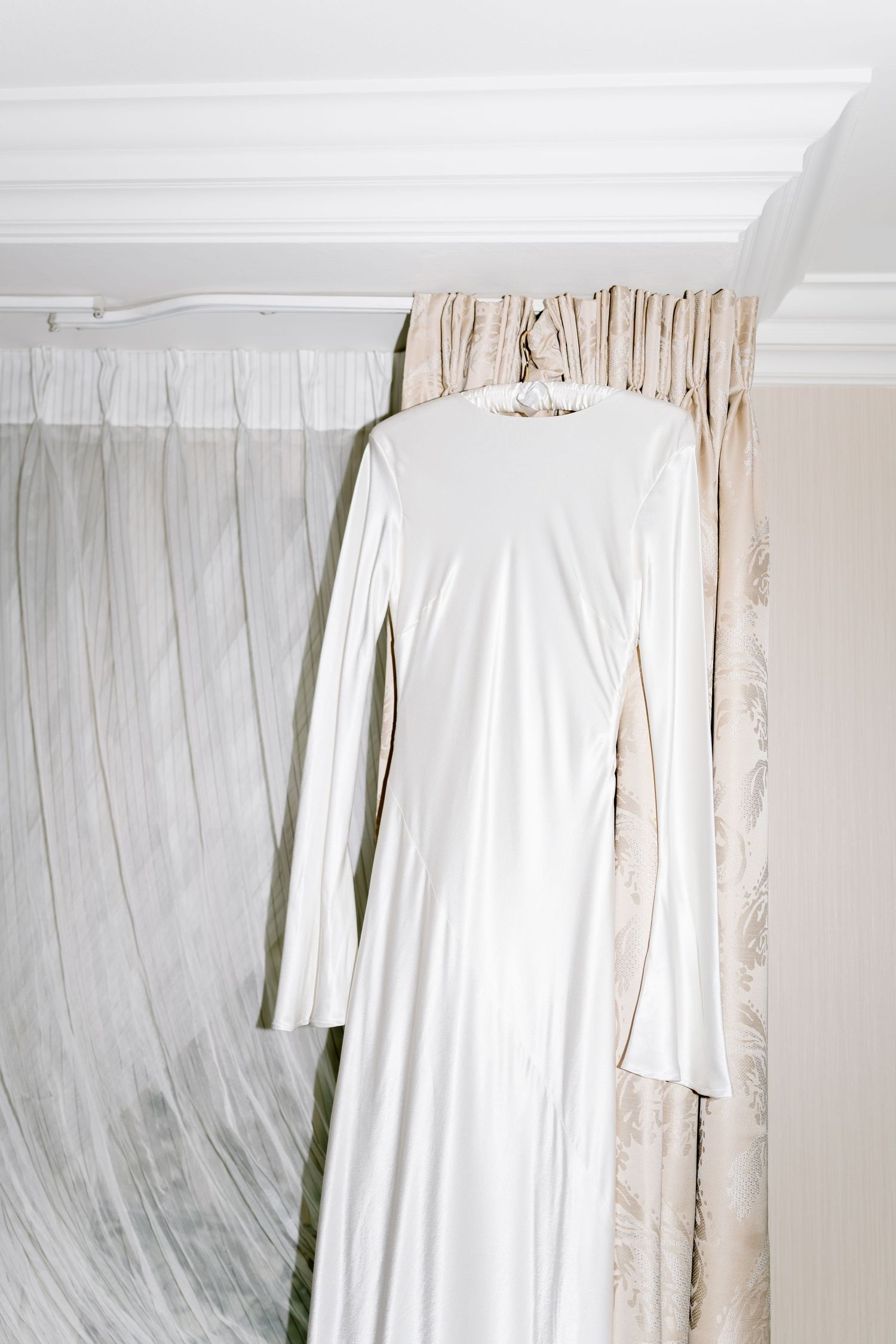 White curtains with delicate pleats hang elegantly against a light-colored wall creating a soft, airy atmosphere.